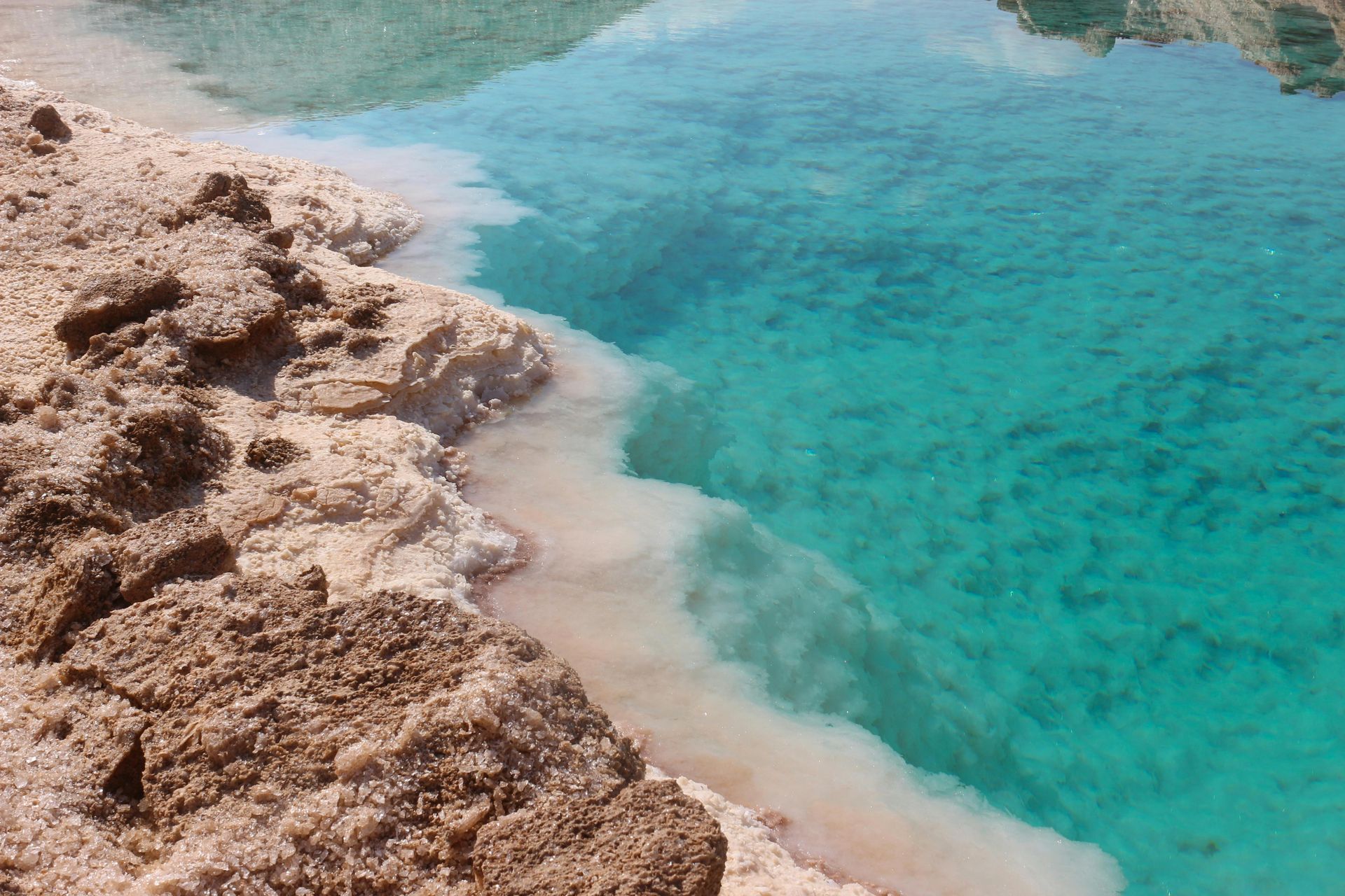 A salt lake with a rocky shoreline and turquoise water at the Siwa Oasis in Egypt.