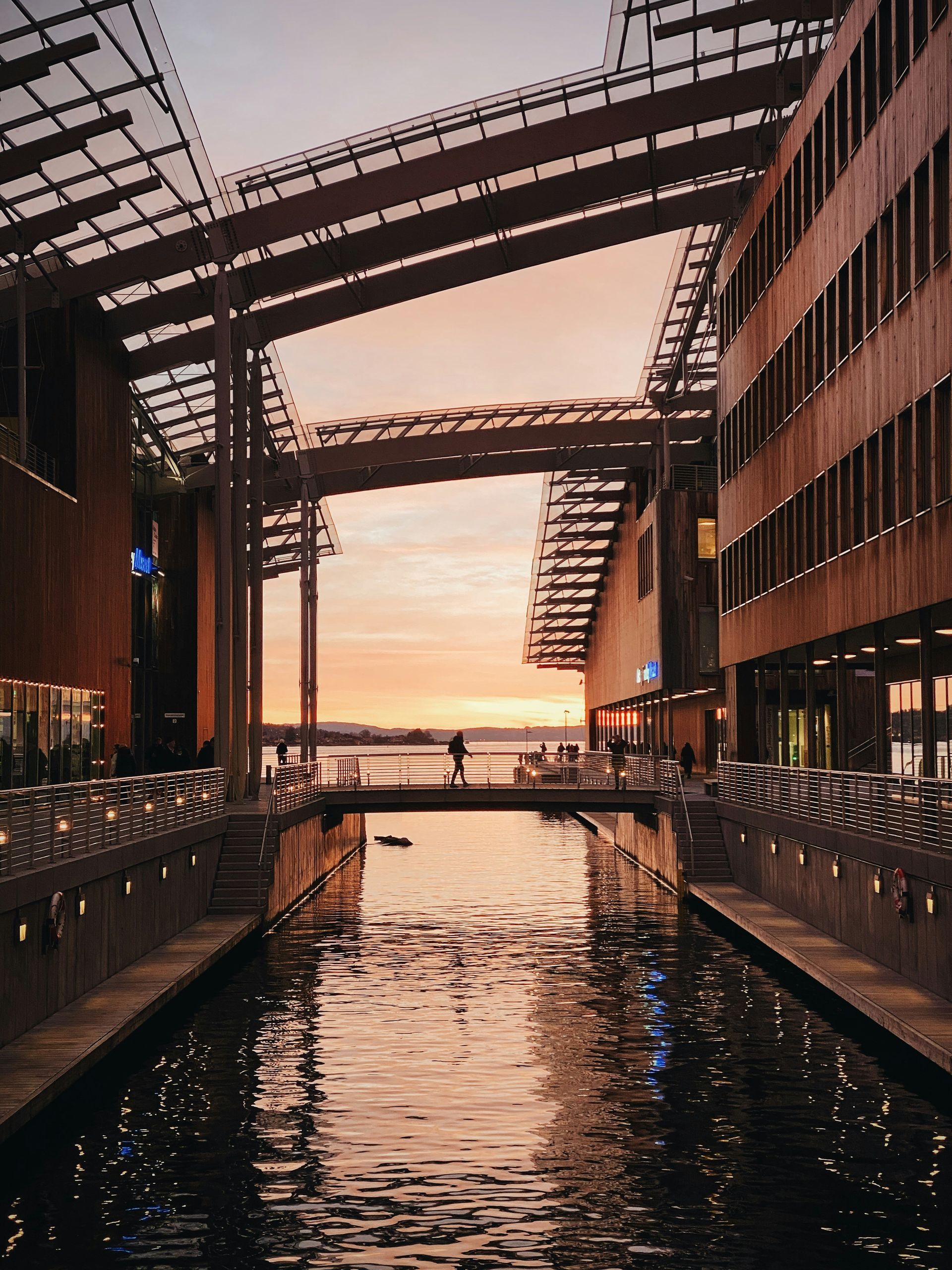 Canal with buildings, a bridge, and a person silhouetted against a sunset in Oslo, Norway.