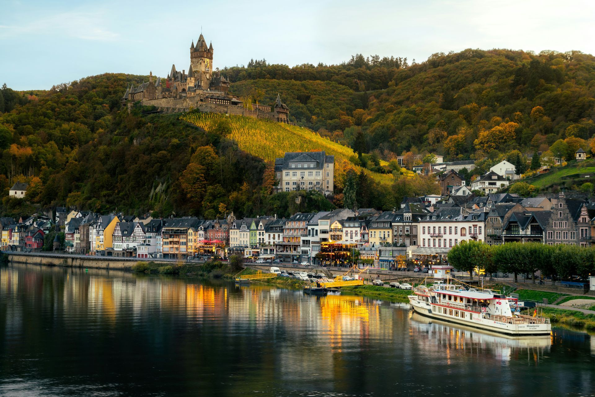 Cochem, Germany, waterfront with colorful buildings, a castle on a hillside, and a boat on the river.