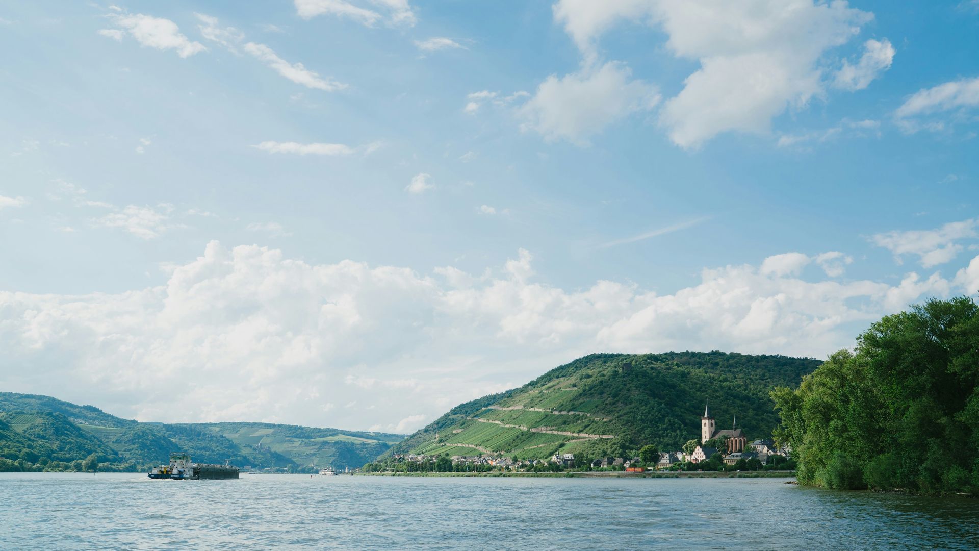 The Rhine River scene with hills, village, and blue sky with clouds in Germany.
