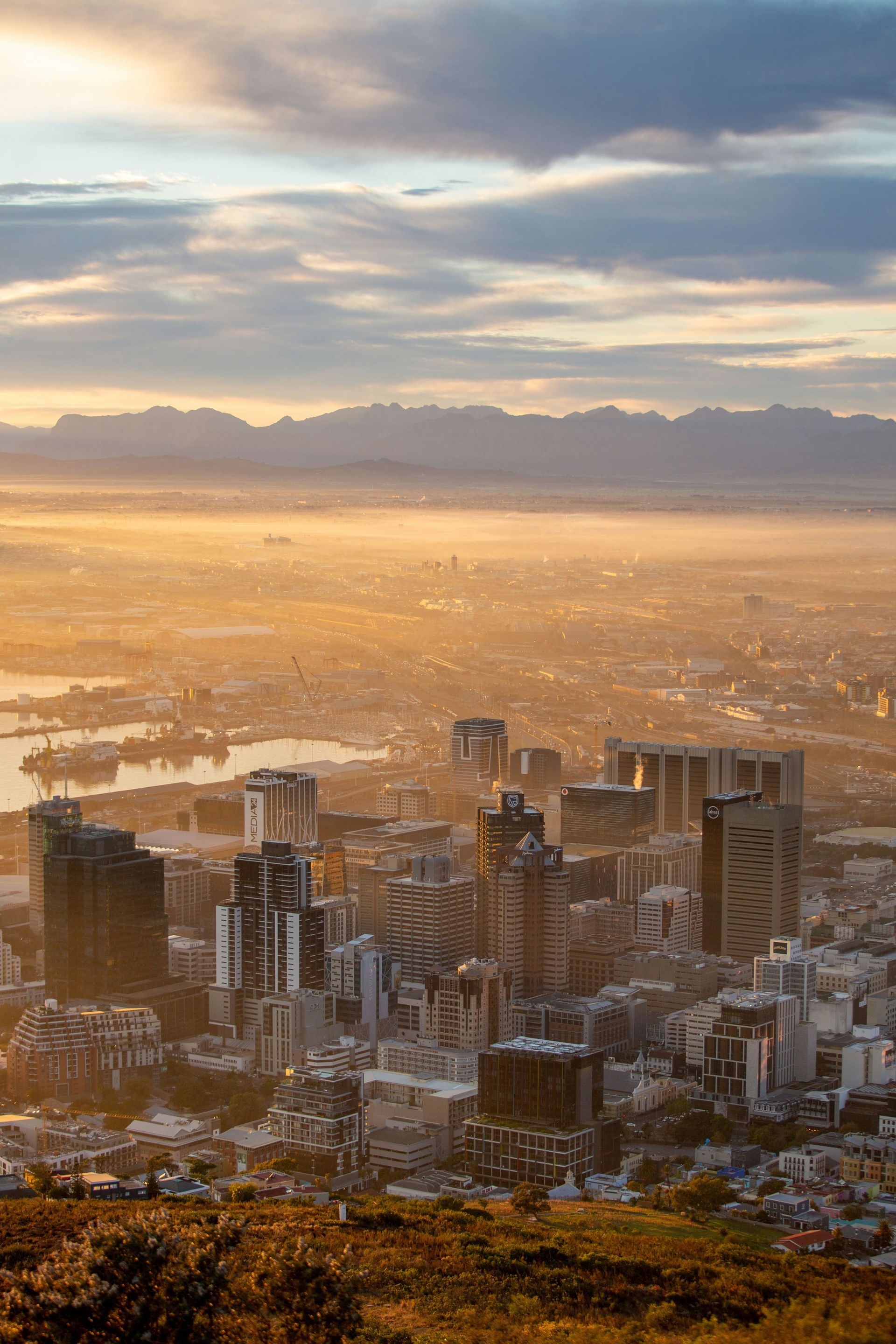 Skyline of Cape Town at sunset, bathed in golden light. Mountains in the distance, hazy clouds above in South Africa.
