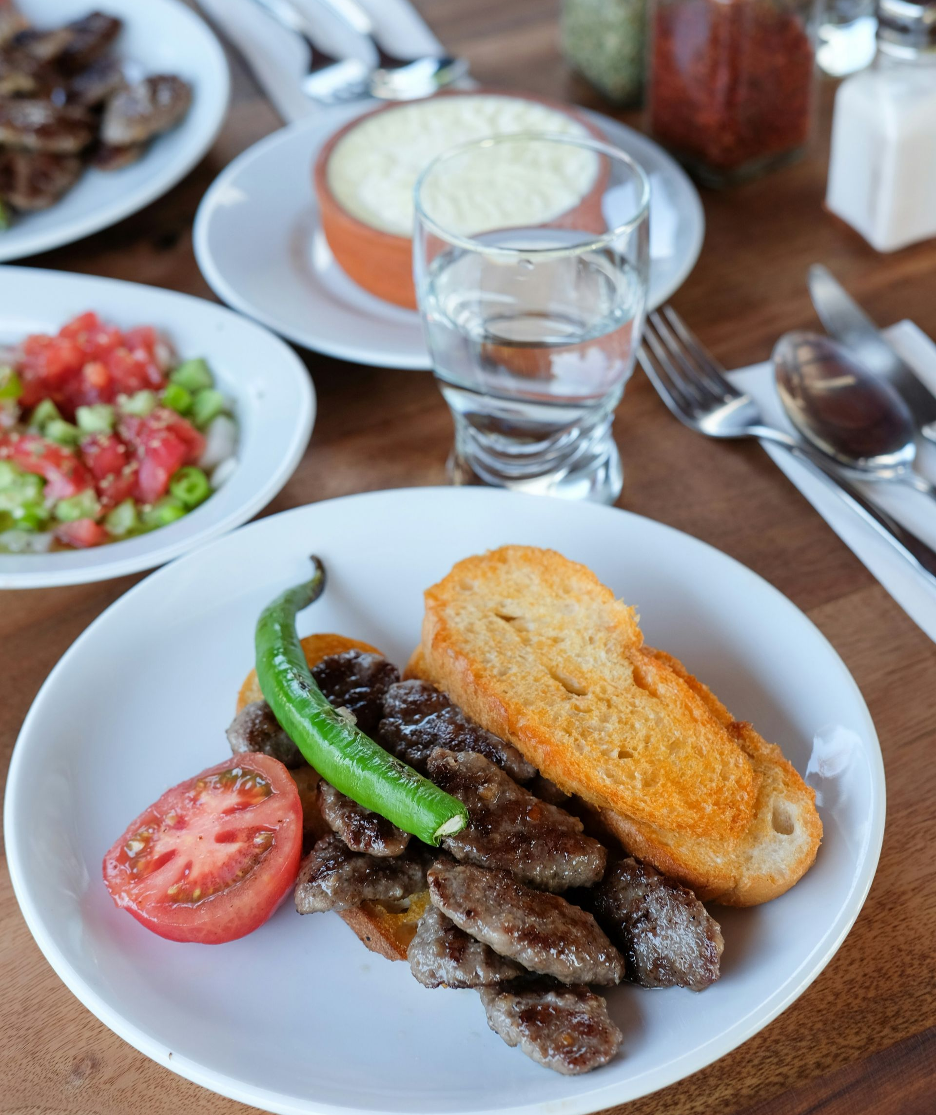 Plate of meatballs, tomato, pepper, and toast with sides of salad and dip on a wooden table in Turkey.