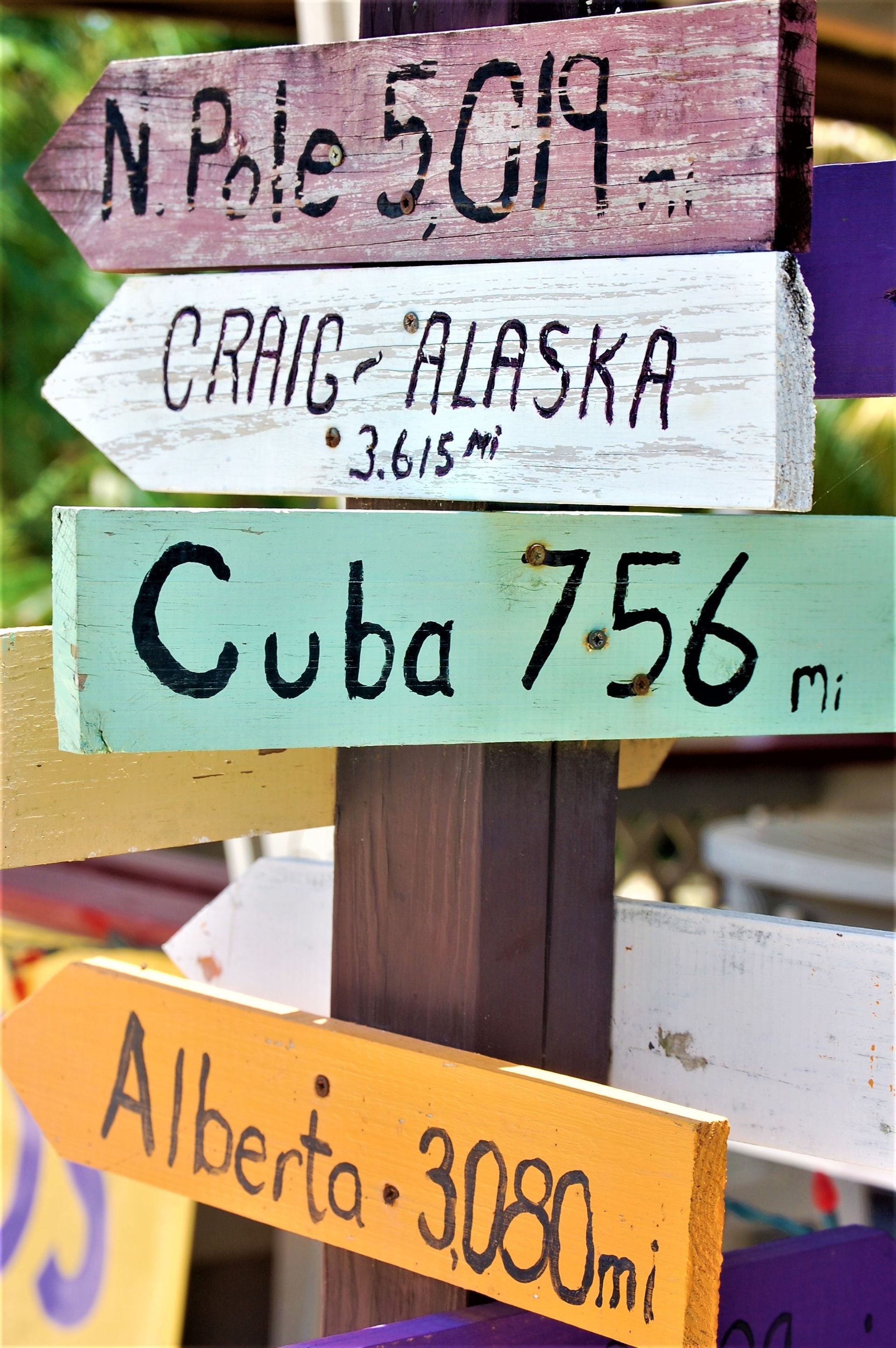 Wooden signpost with colorful arrows pointing to various locations, including Craig, Alaska, and Cuba in Placencia, Belize.