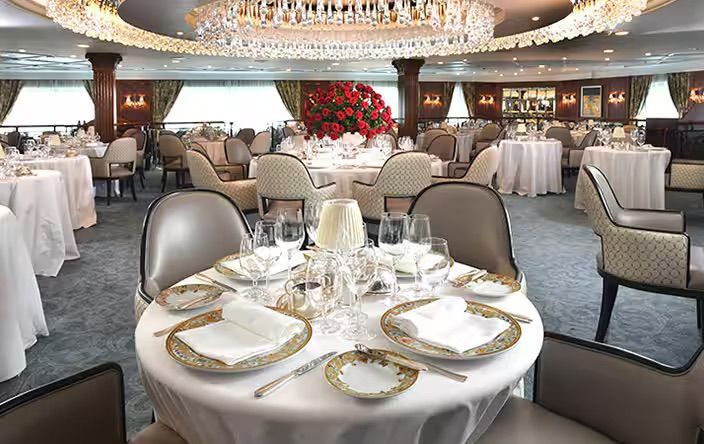 A large dining room with tables and chairs and a chandelier on the Oceania Insignia cruise ship.