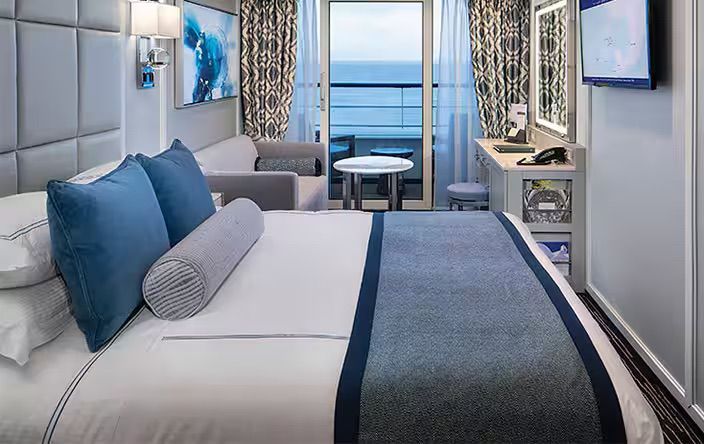 A hotel room with a large bed and a balcony overlooking the ocean, on the Oceania Insignia cruise ship.