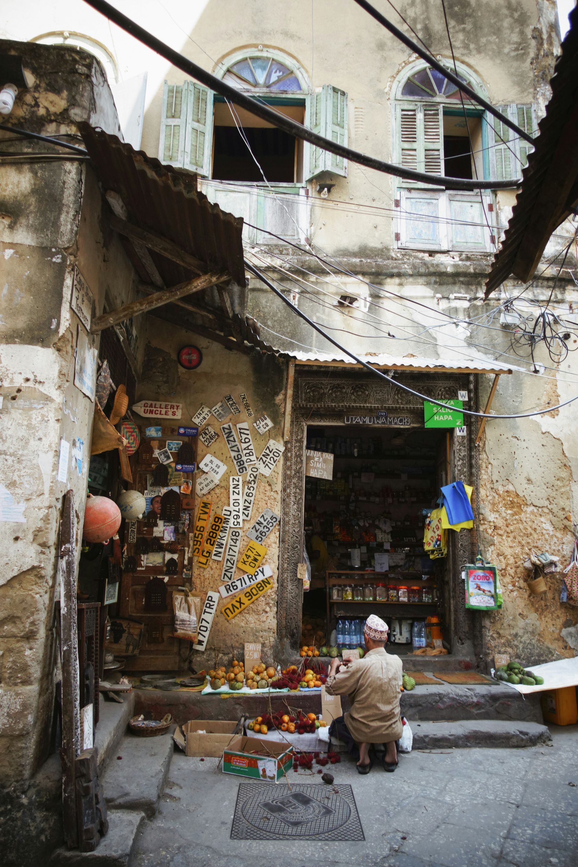 A man is sitting in front of a store selling fruits and vegetables in Zanzibar, Tanzania.