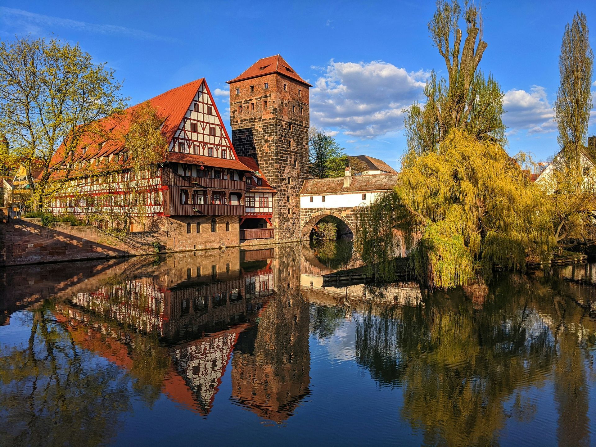 Waterfront view of Nuremberg, Germany, with historic buildings, reflection in water, and blue sky.