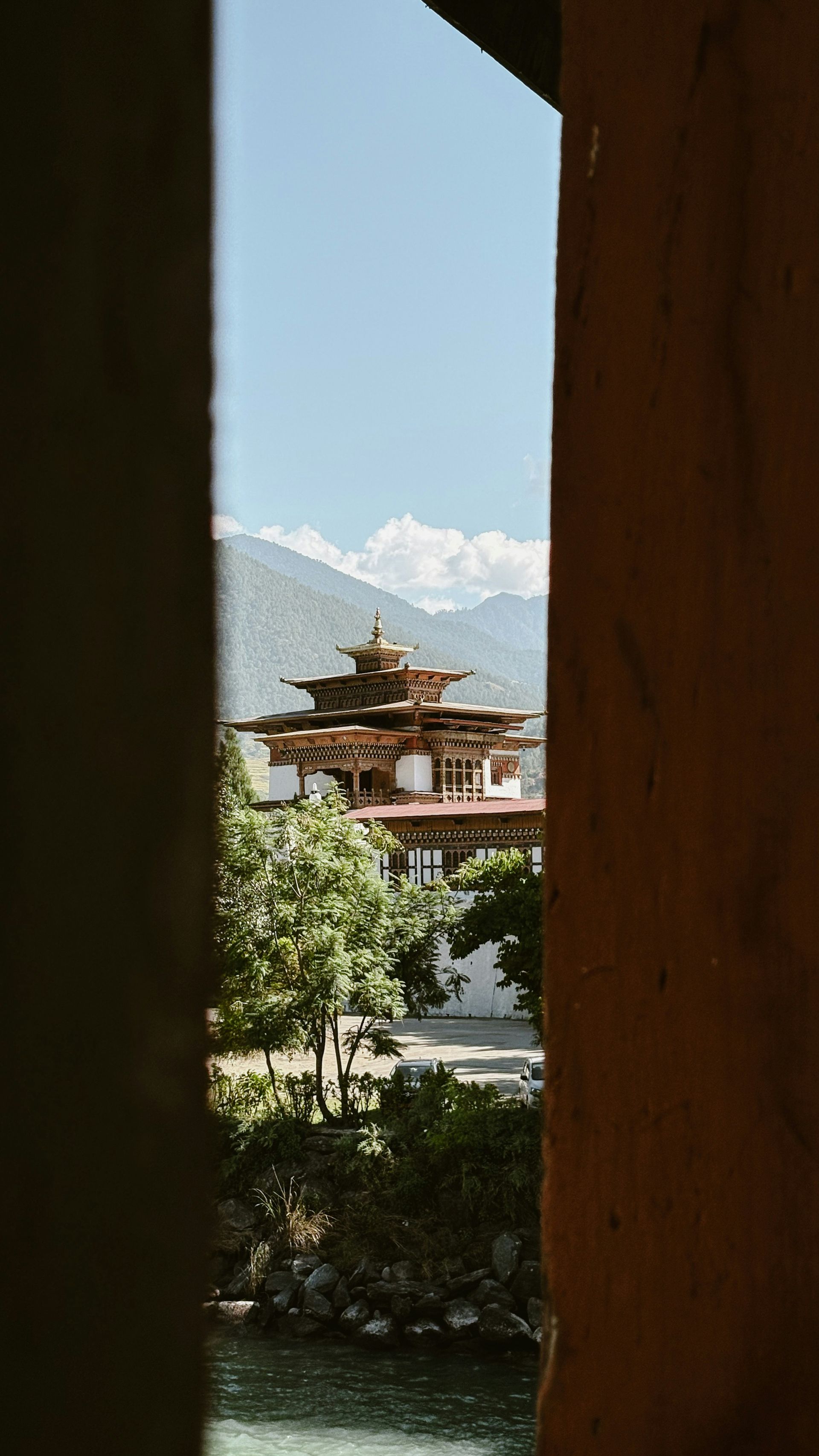 View of Punakha Dzong framed by a window, with mountains in Punakha, Bhutan.