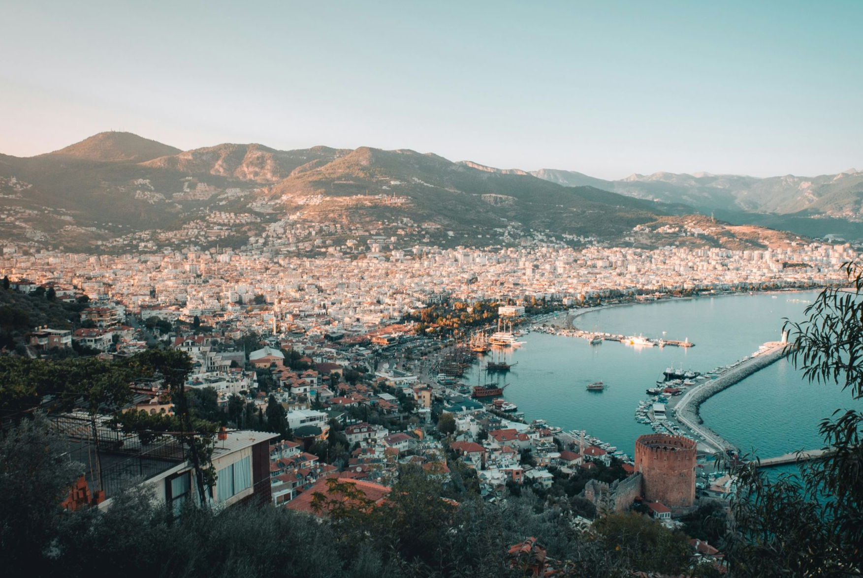 Coastal city with a harbor, surrounded by mountains. Buildings sprawl along the coast in Turkey.