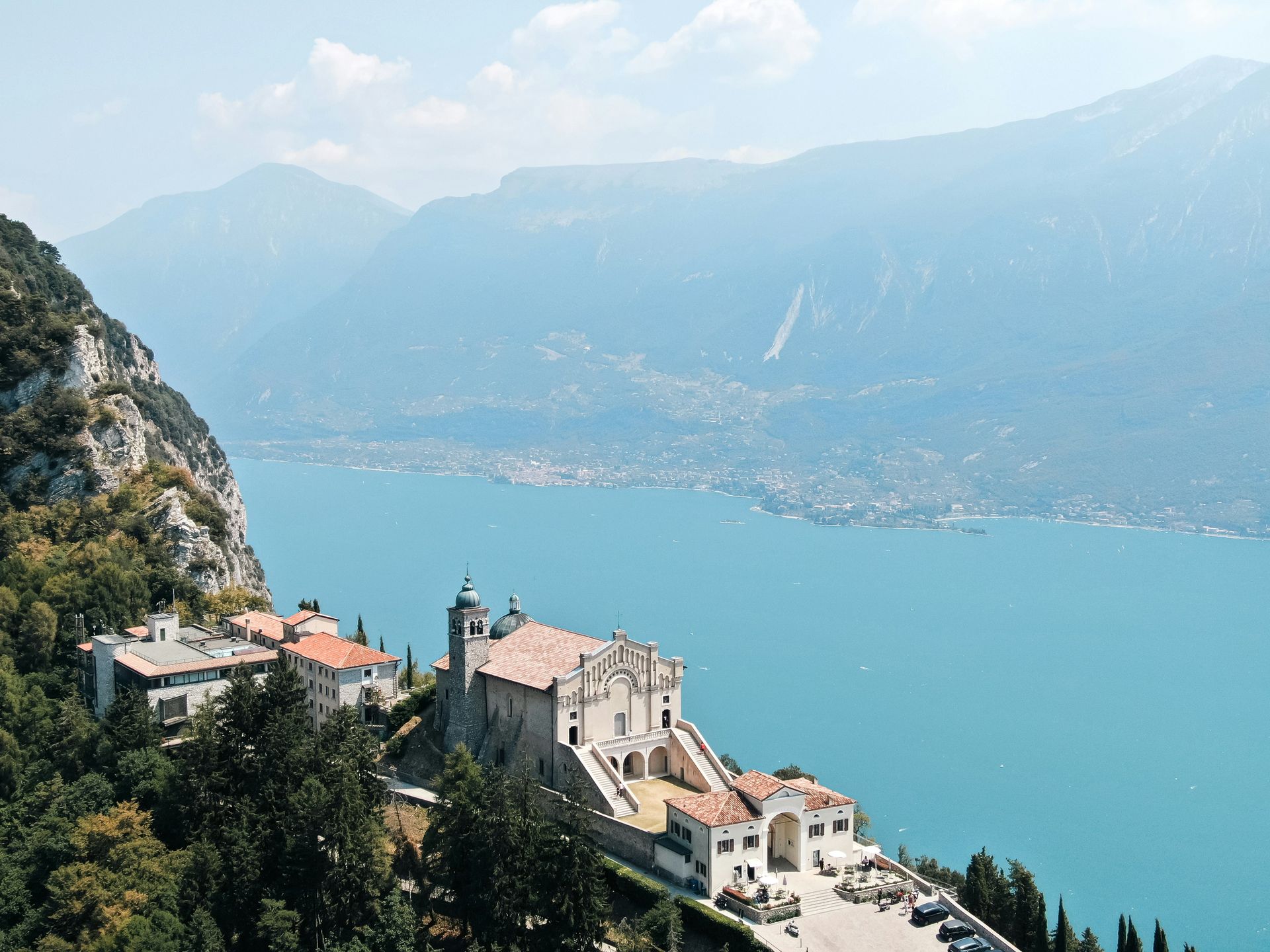 An aerial view of a castle on top of a hill overlooking Lake Garda, surrounded by mountains in Italy.
