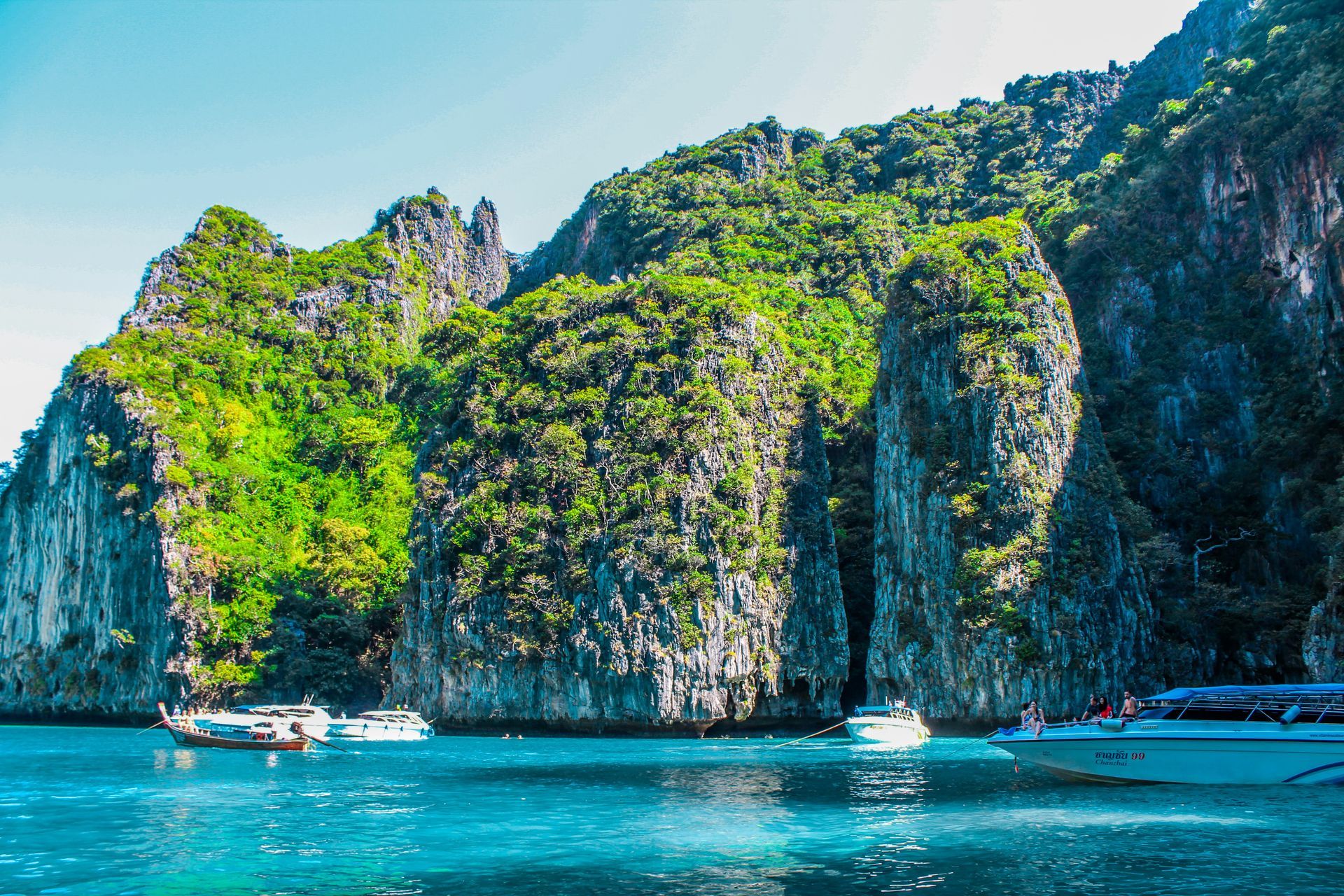 A group of boats are floating on top of a body of water surrounded by the Phi Phi Islands in Krabi, Thailand.