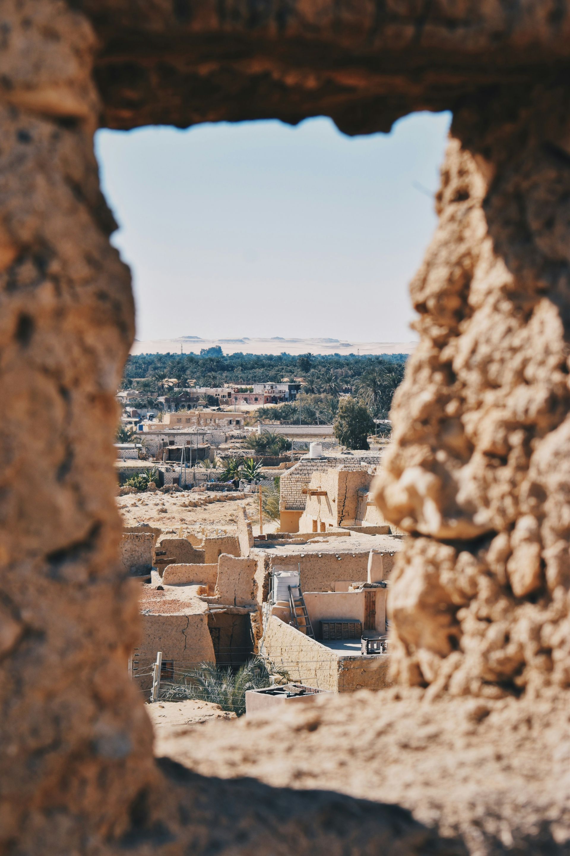 A view of a city through a hole in a stone wall in Siwa, Egypt.