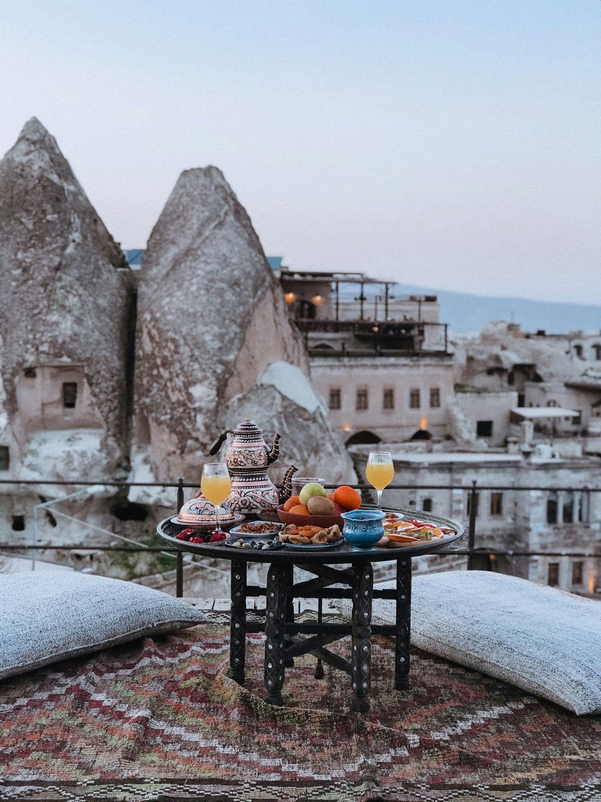 Breakfast table with food and drinks on a rooftop with rock formations and buildings in Cappadocia, Turkey.