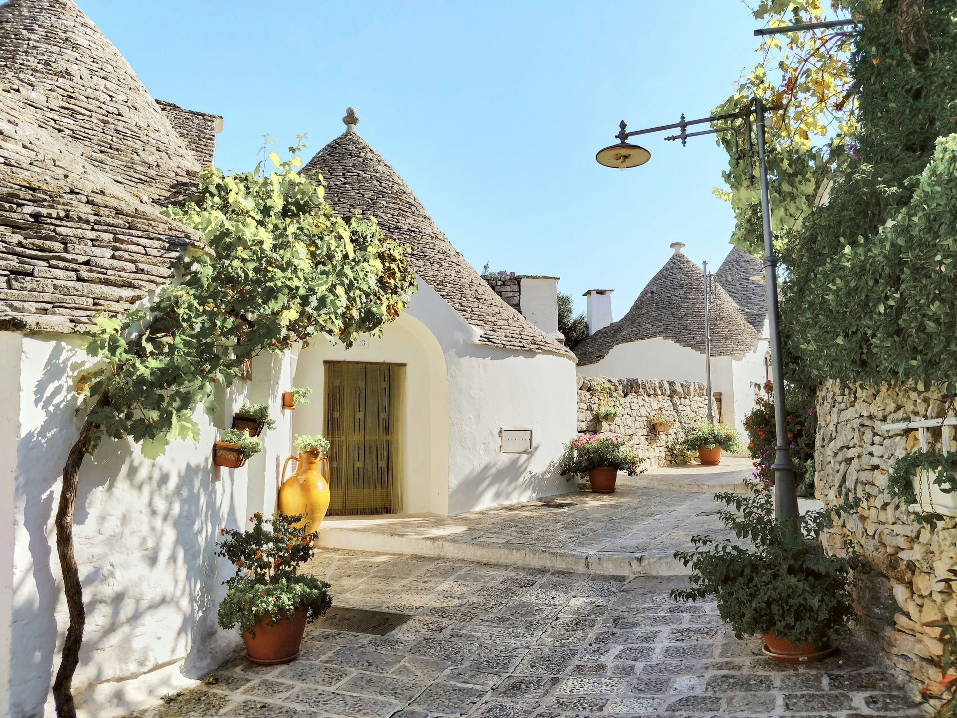 A row of white houses with a thatched roof is lined up on a cobblestone street in Alberobello, Italy.