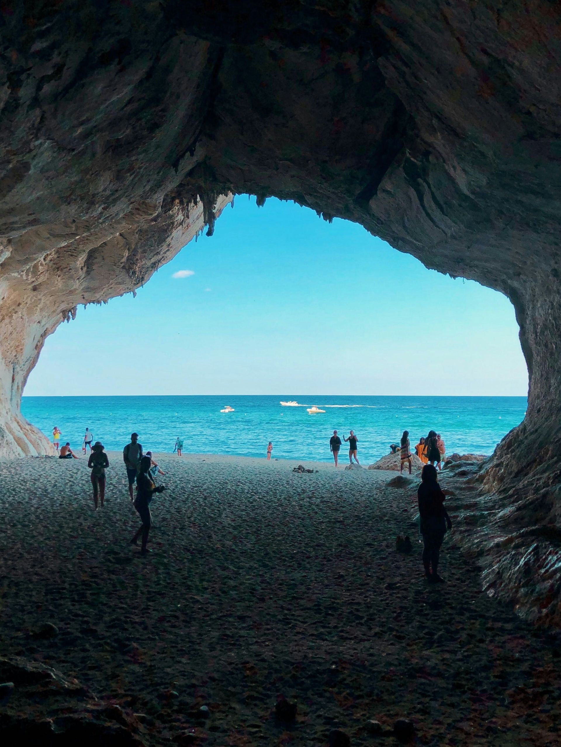 A group of people are standing in a cave overlooking the ocean in Sardinia, Italy.