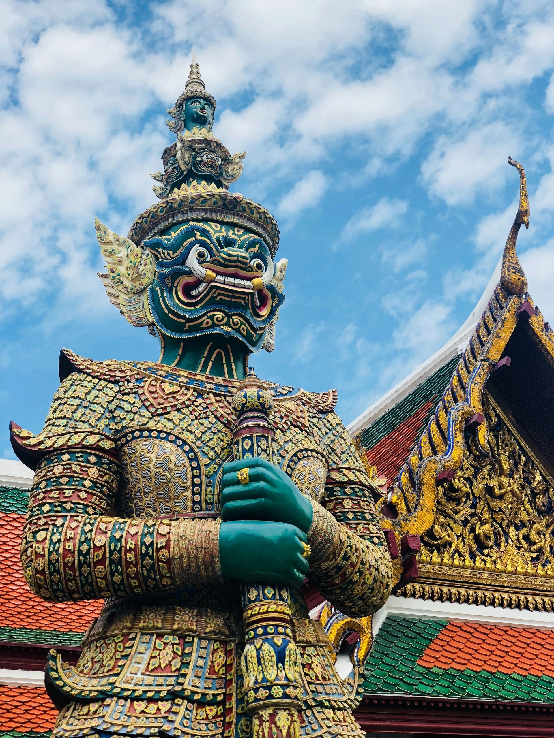 A statue of a giant man with a mask is standing in front of a building in Bangkok, Thailand.