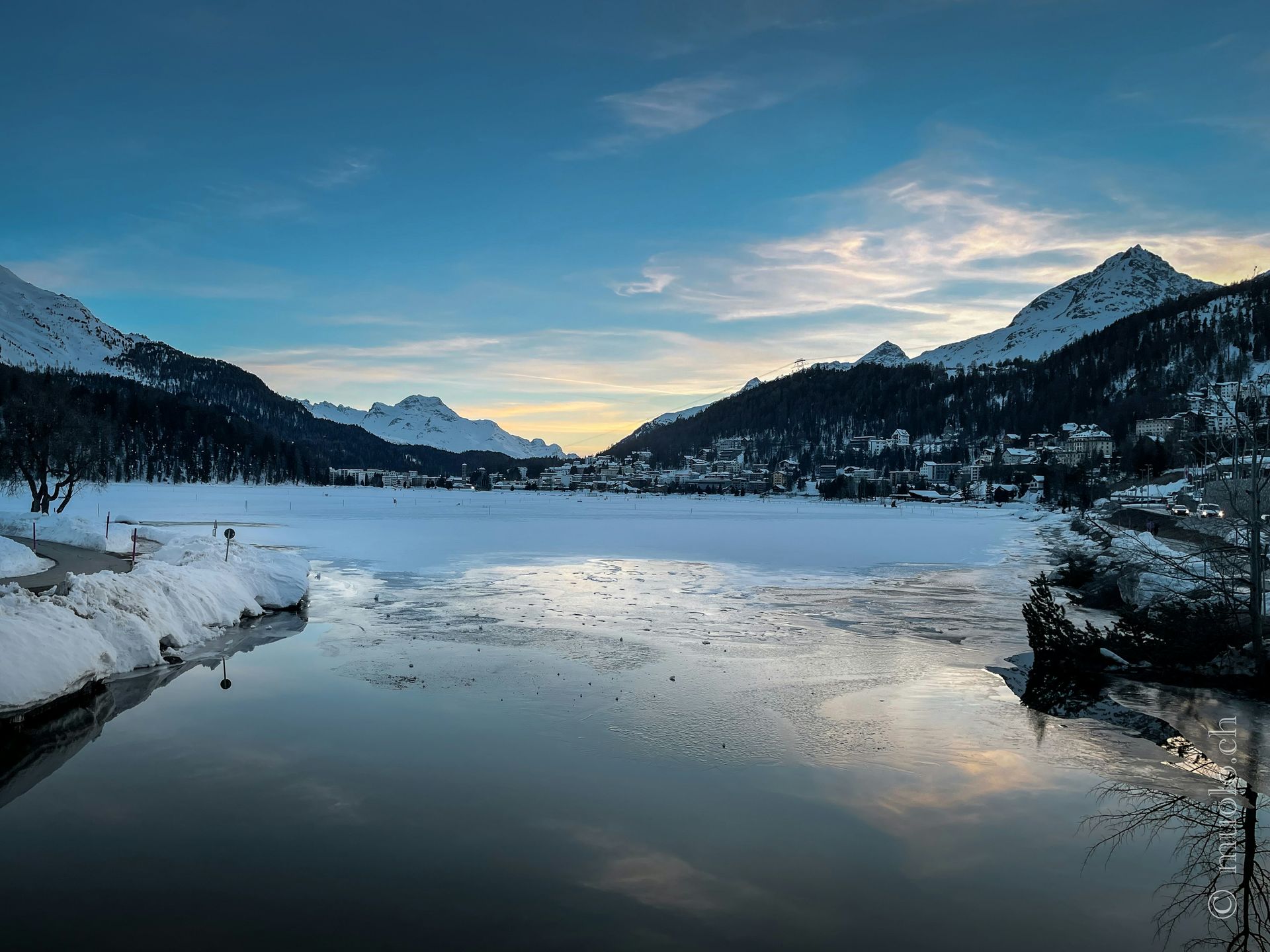 Snowy mountain lake at sunset, mountains frame the horizon, with clear water in the foreground in St. Moritz, Switzerland. 