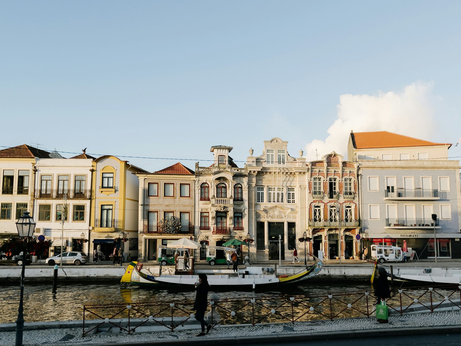 Colorful buildings line a canal in Aveiro, Portugal. People walk by; a boat floats.