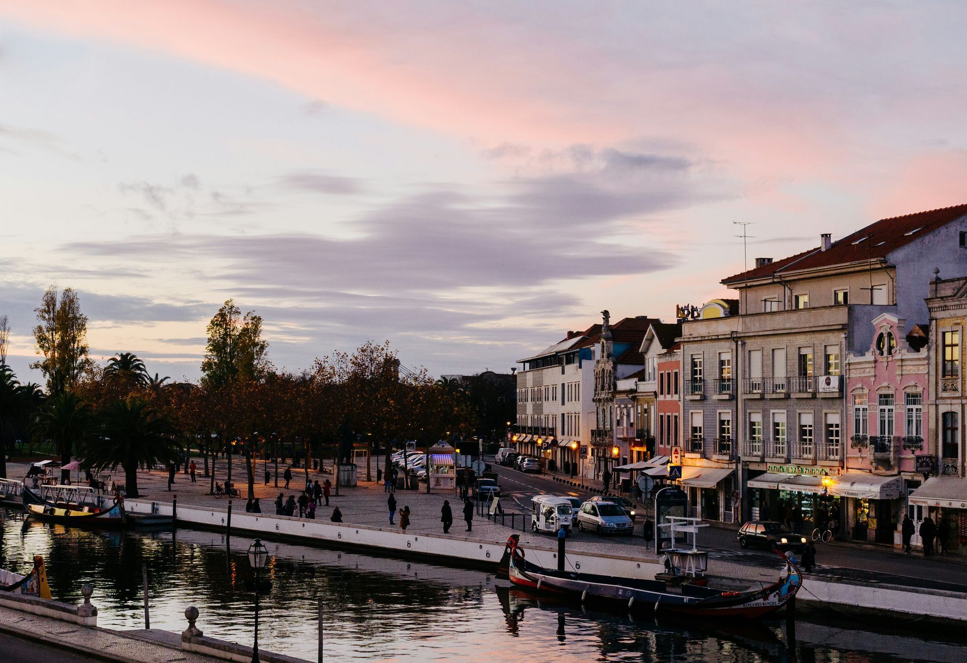 Canal with gondola in Aveiro, Portugal, at dusk. Buildings line the water, pink and purple sky.