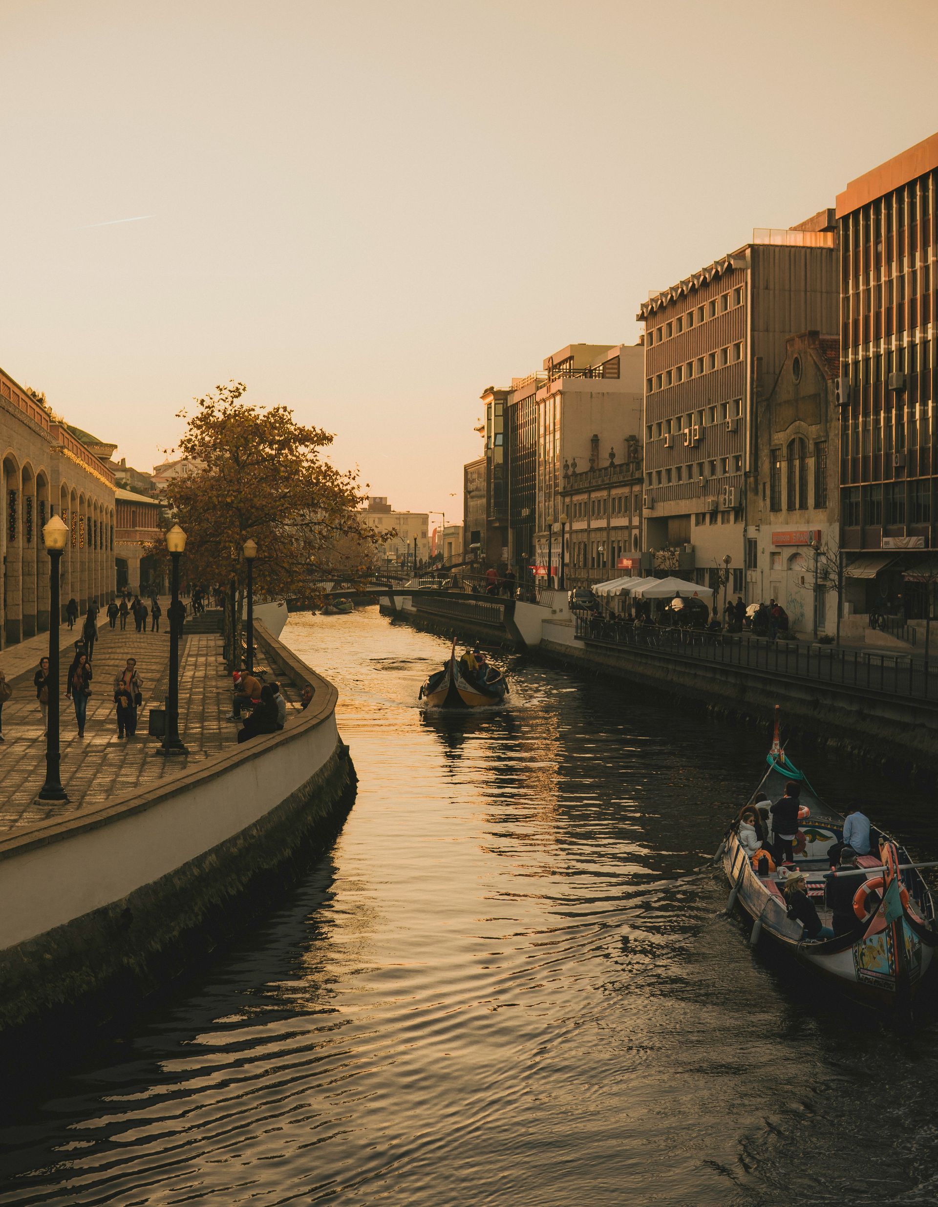 Canal with boats and buildings at sunset. People on the walkway in Aveiro, Portugal.