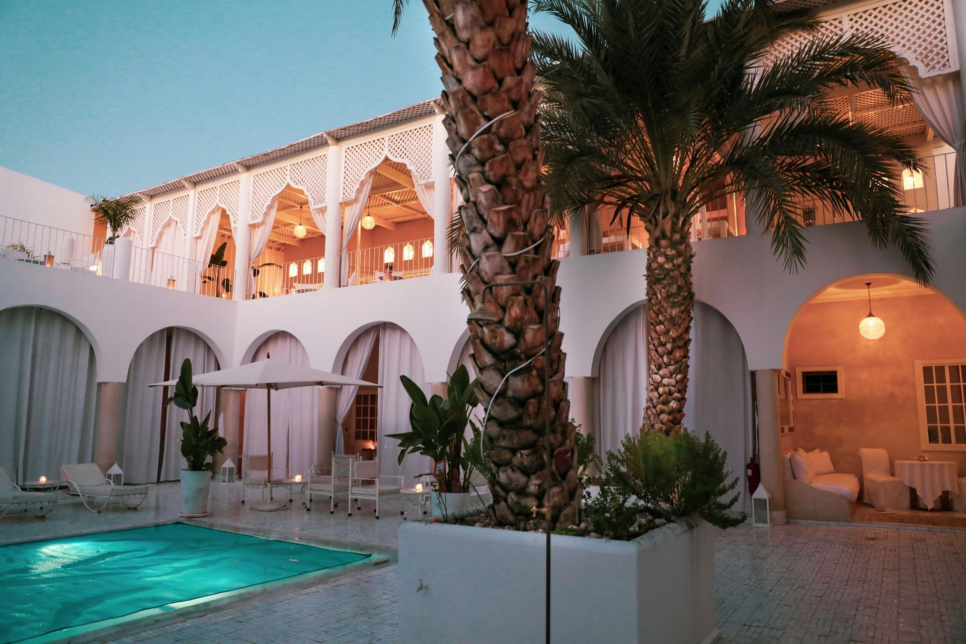 A large white riad with a swimming pool and palm trees in front of it in Marrakesh, Morocco.