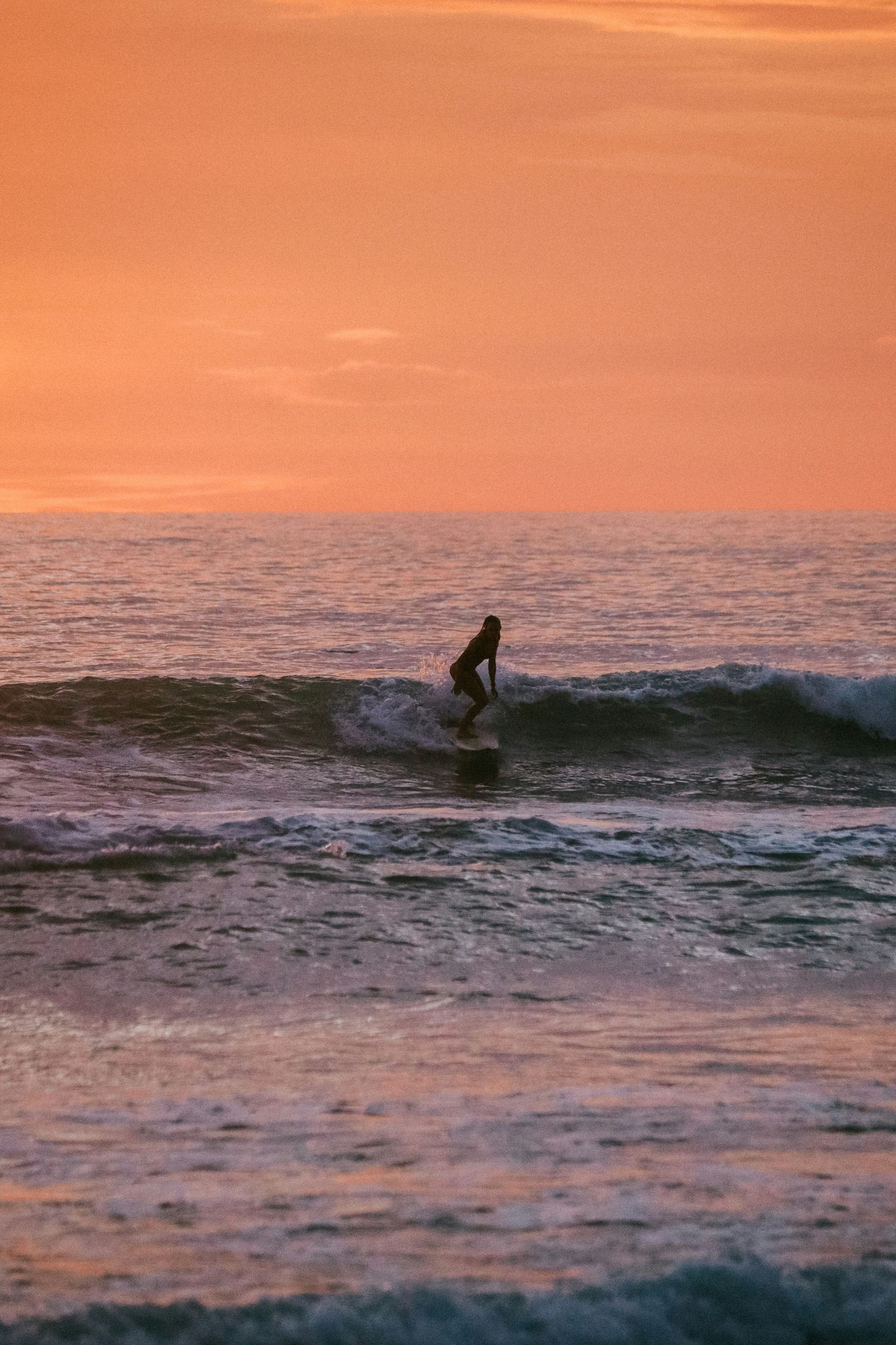 A surfer riding a wave at sunset; orange sky reflected in the ocean in Tamarindo, Costa Rica.