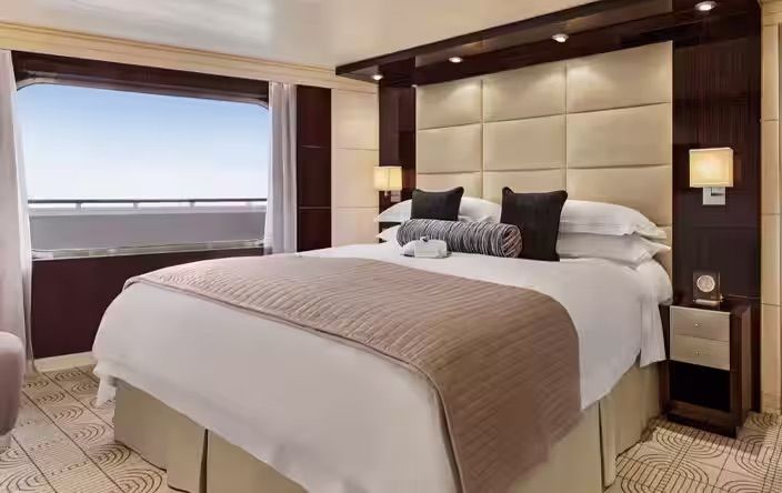 A hotel room with a large bed and a large window on the Oceania Riviera cruise ship.