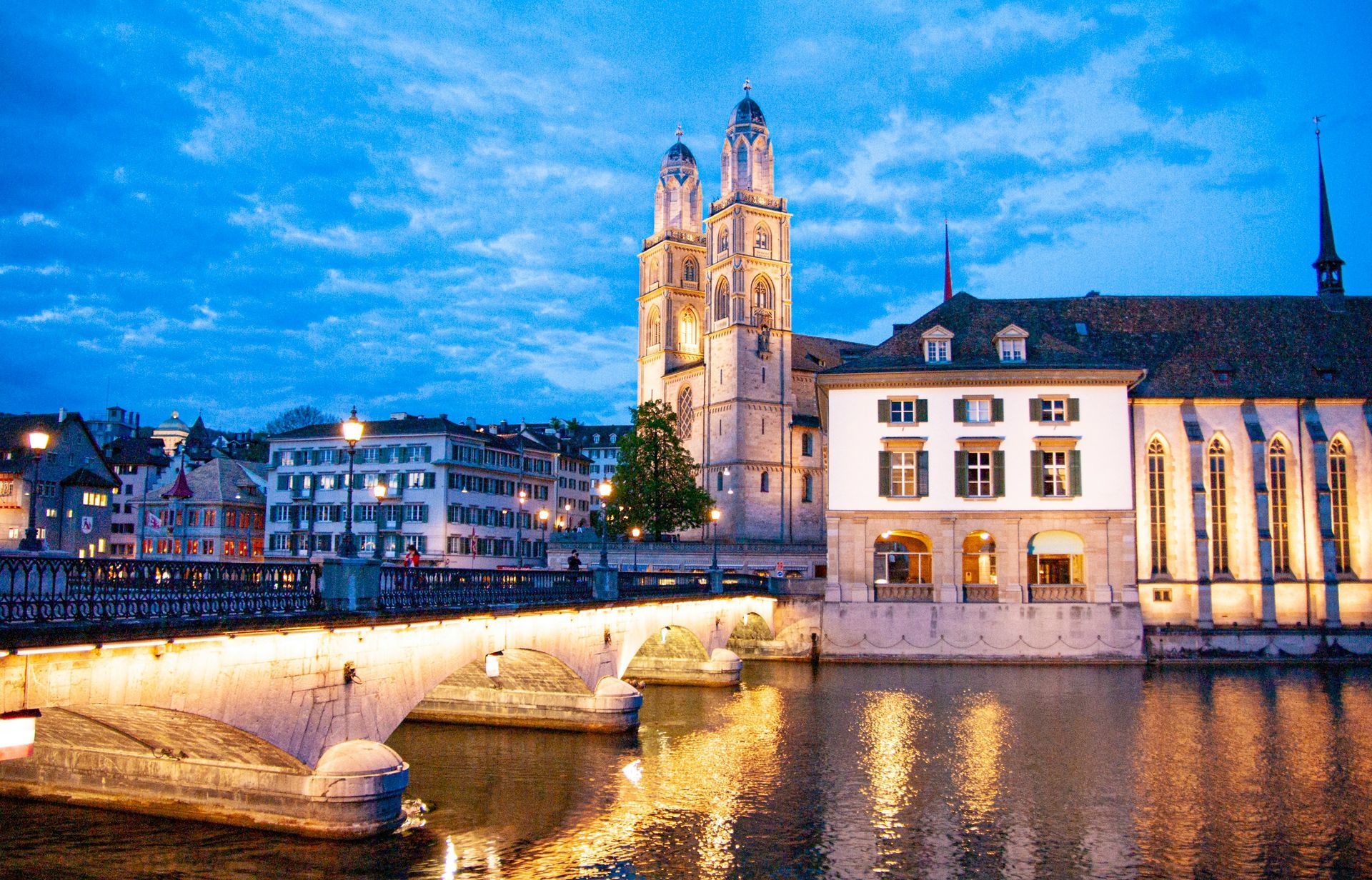 Evening view of Zurich, Switzerland. Bridge over river with illuminated buildings and church.