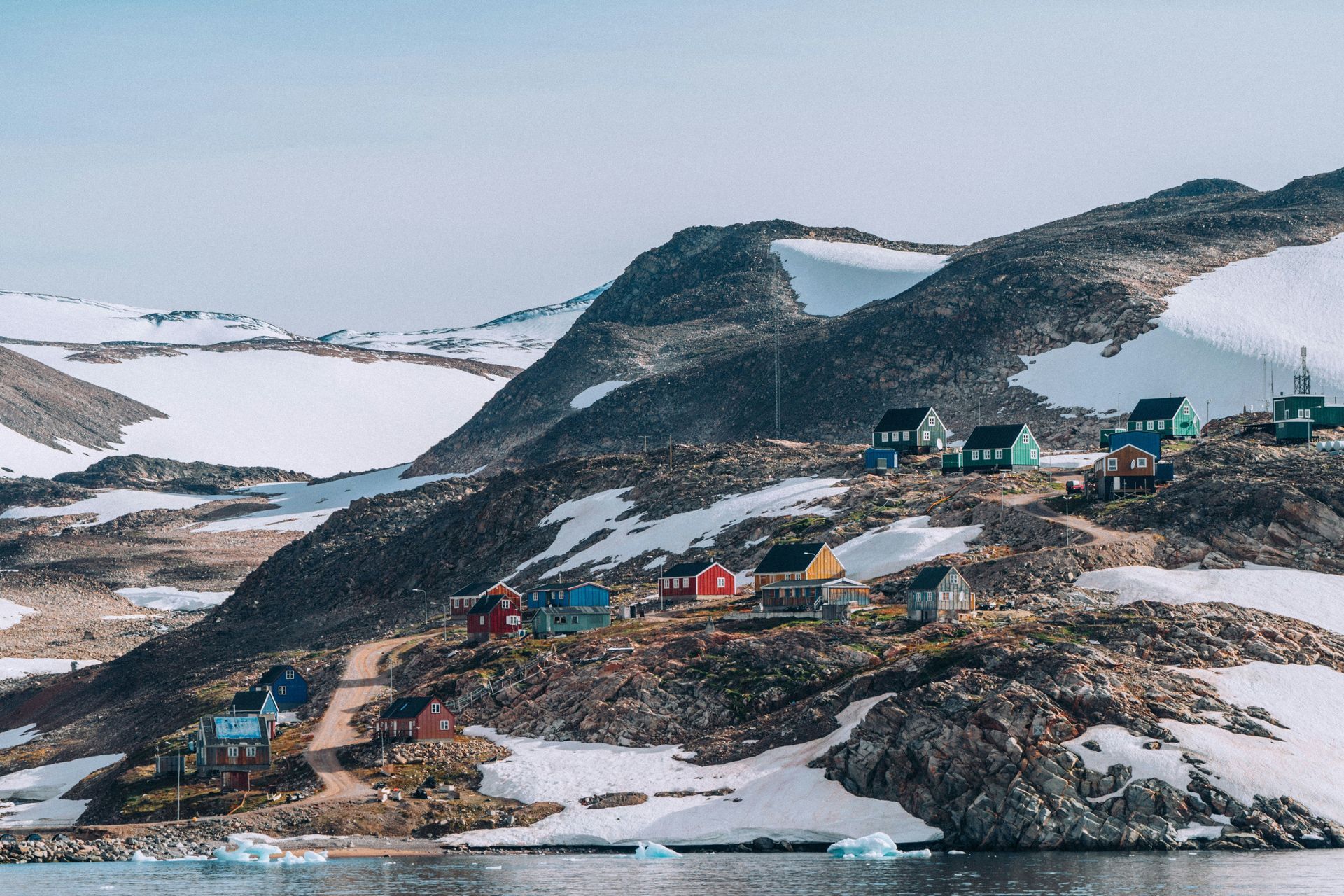 Colorful houses on a rocky hillside with snow, overlooking water in Ittoqqortoormiit, Greenland.