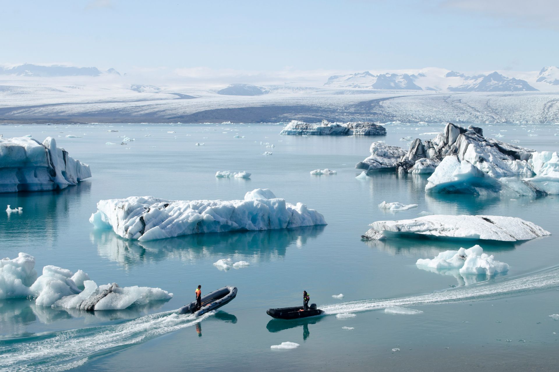 Two boats navigate Jökulsárlón Glacier Lagoon in Iceland, snow-capped mountains in the background.