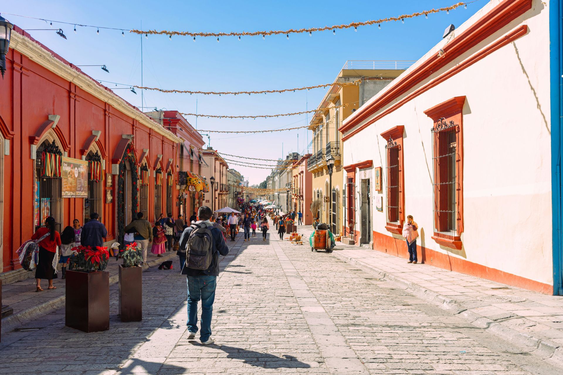 Street scene in Oaxaca, Mexico, with colorful buildings, cobblestone road, and people walking.