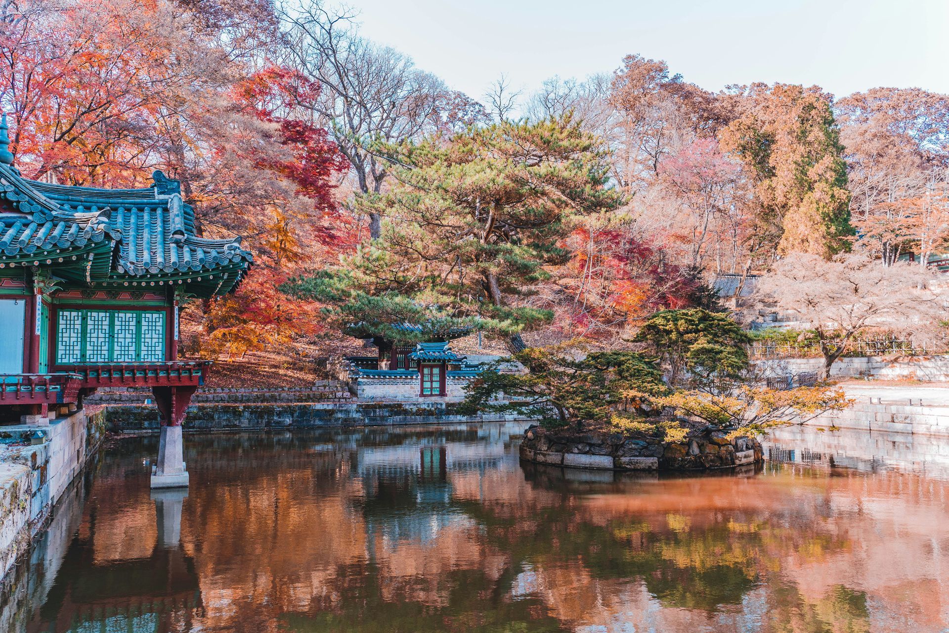 Autumnal scene of Changdeokgung Palace by a calm lake, surrounded by colorful trees in South Korea.