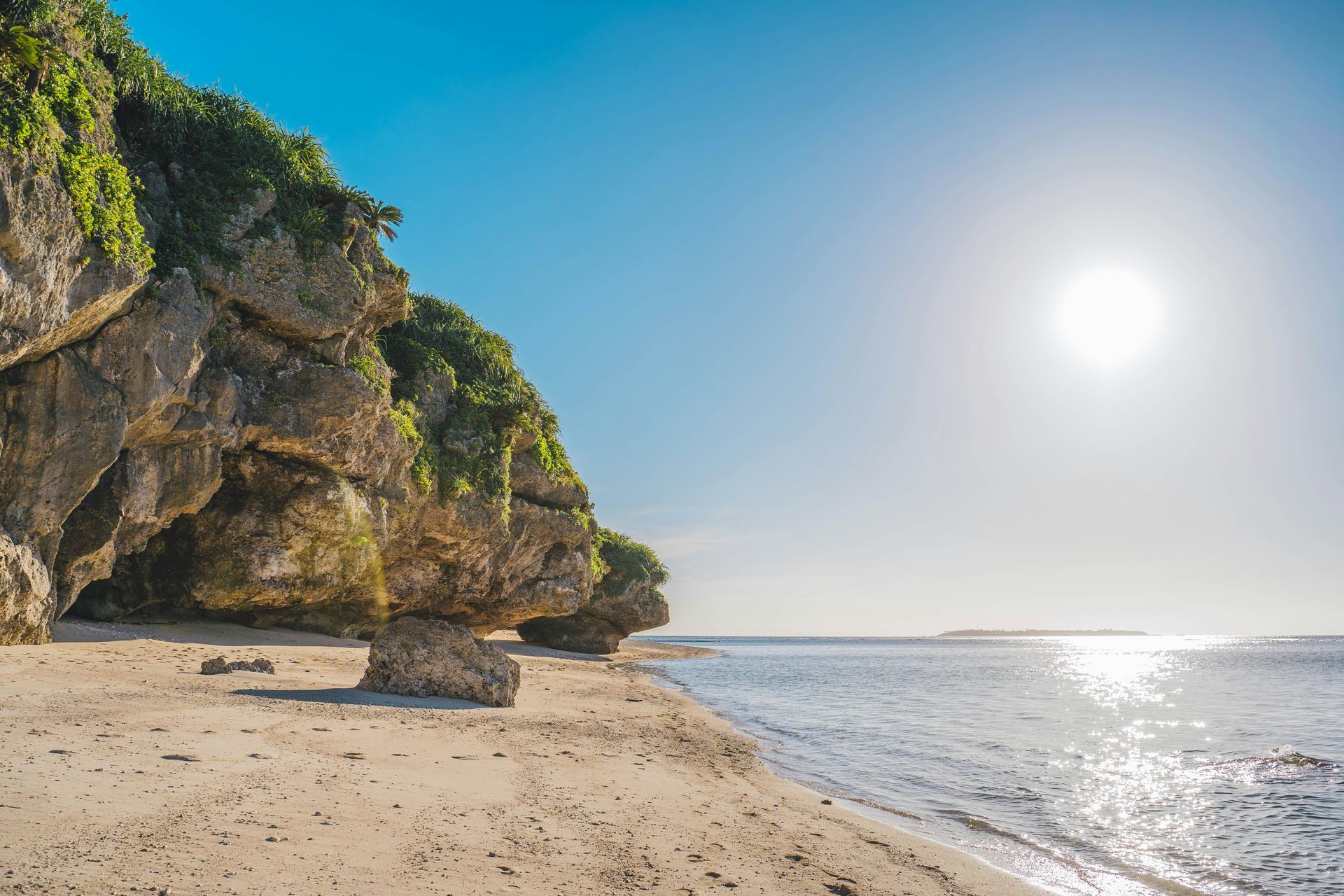 Rocky cliffs with greenery overhang a sandy beach in Okinawa, Japan.