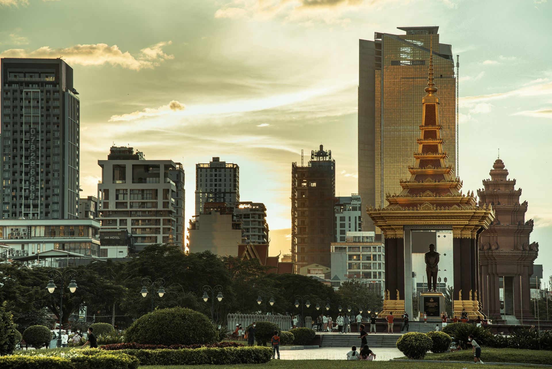 Phnom Penh skyline with modern buildings, a golden monument backlit by a sunset in Cambodia.
