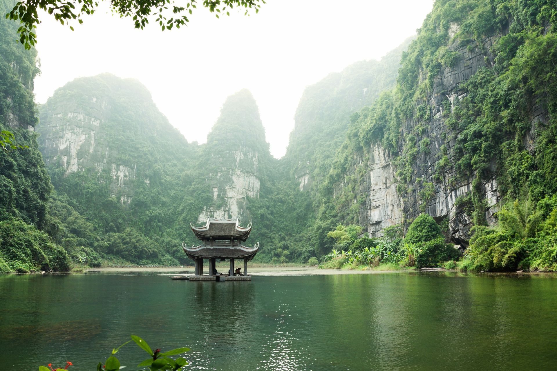 Lake with pagoda surrounded by lush, green cliffs in Ninh Bình, Vietnam.