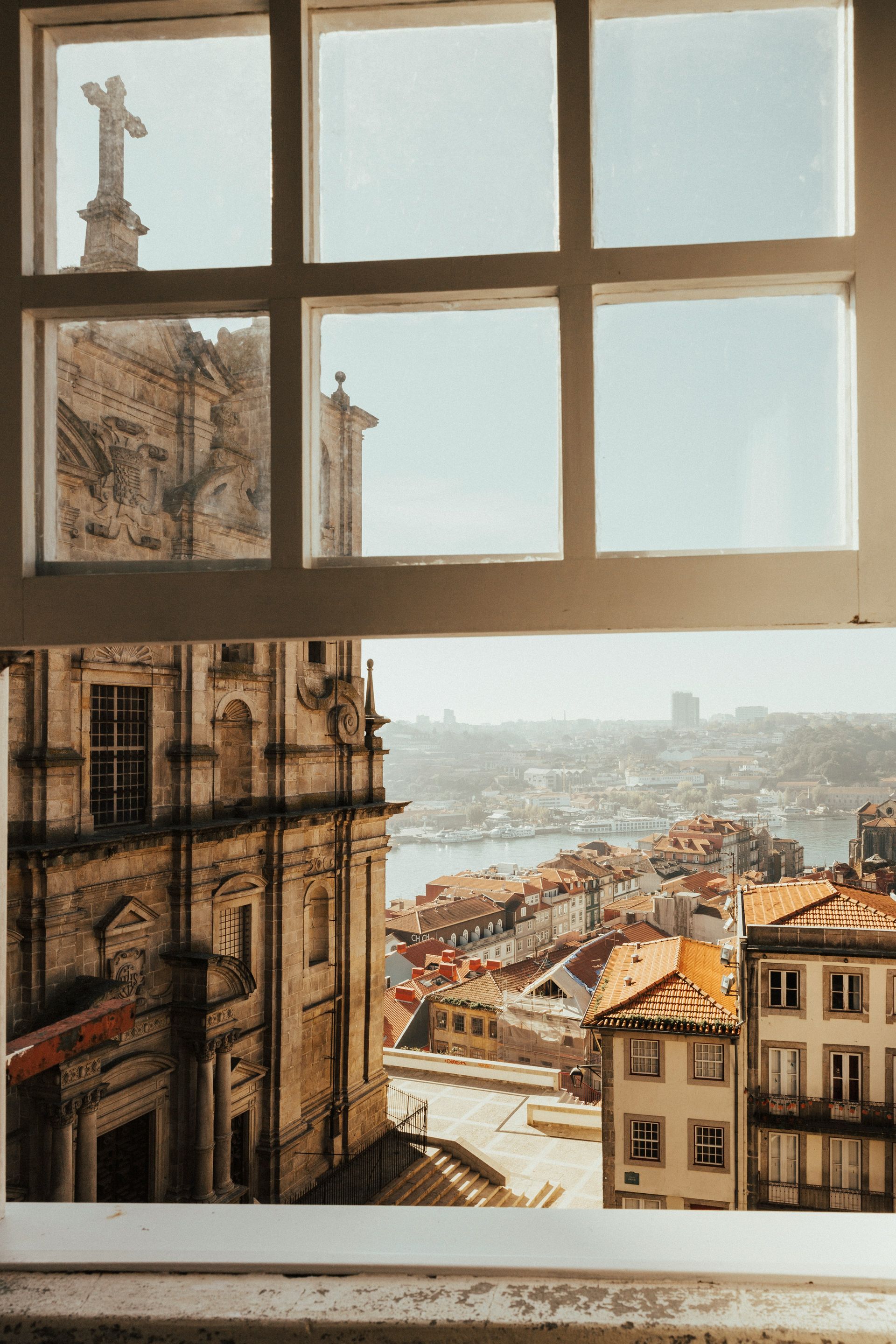 View through a window of a city with a church and cross on a sunny day in Porto, Portugal.
