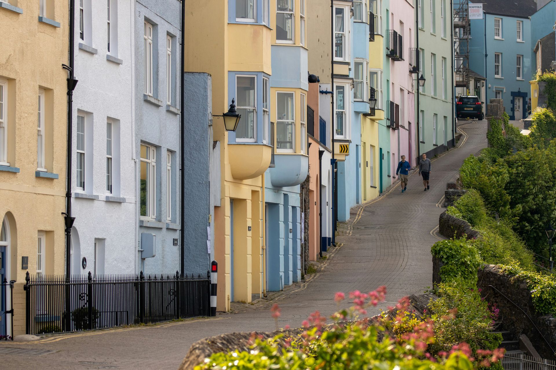 Colorful row of houses on a sloped street, two people walking in Tenby, Wales.