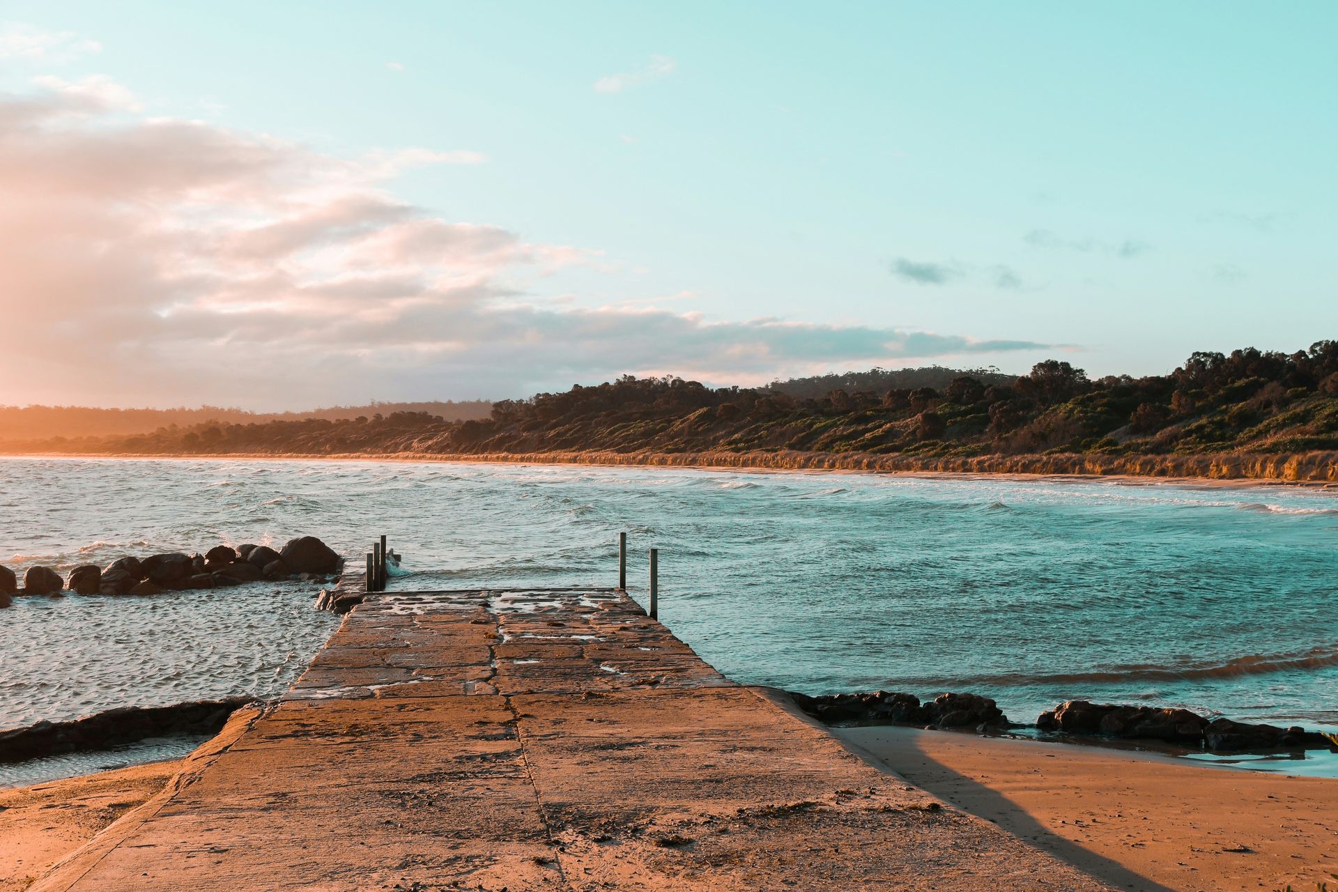 A pier leading into a body of water with a sunset in the background in Tasmania, Australia.