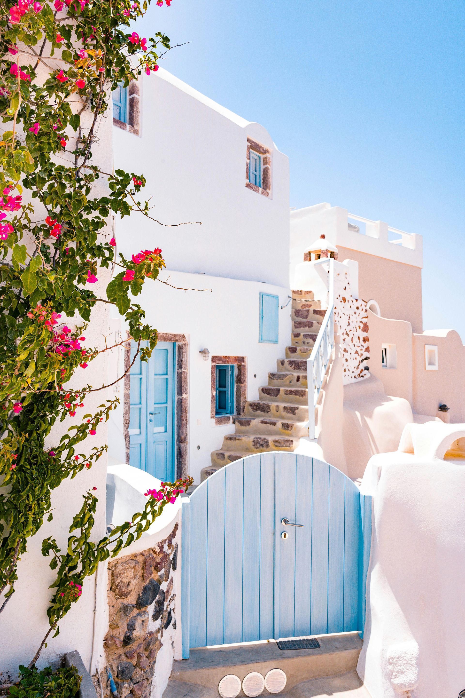 A white building with a blue door and stairs leading up to it in Santorini, Greece.