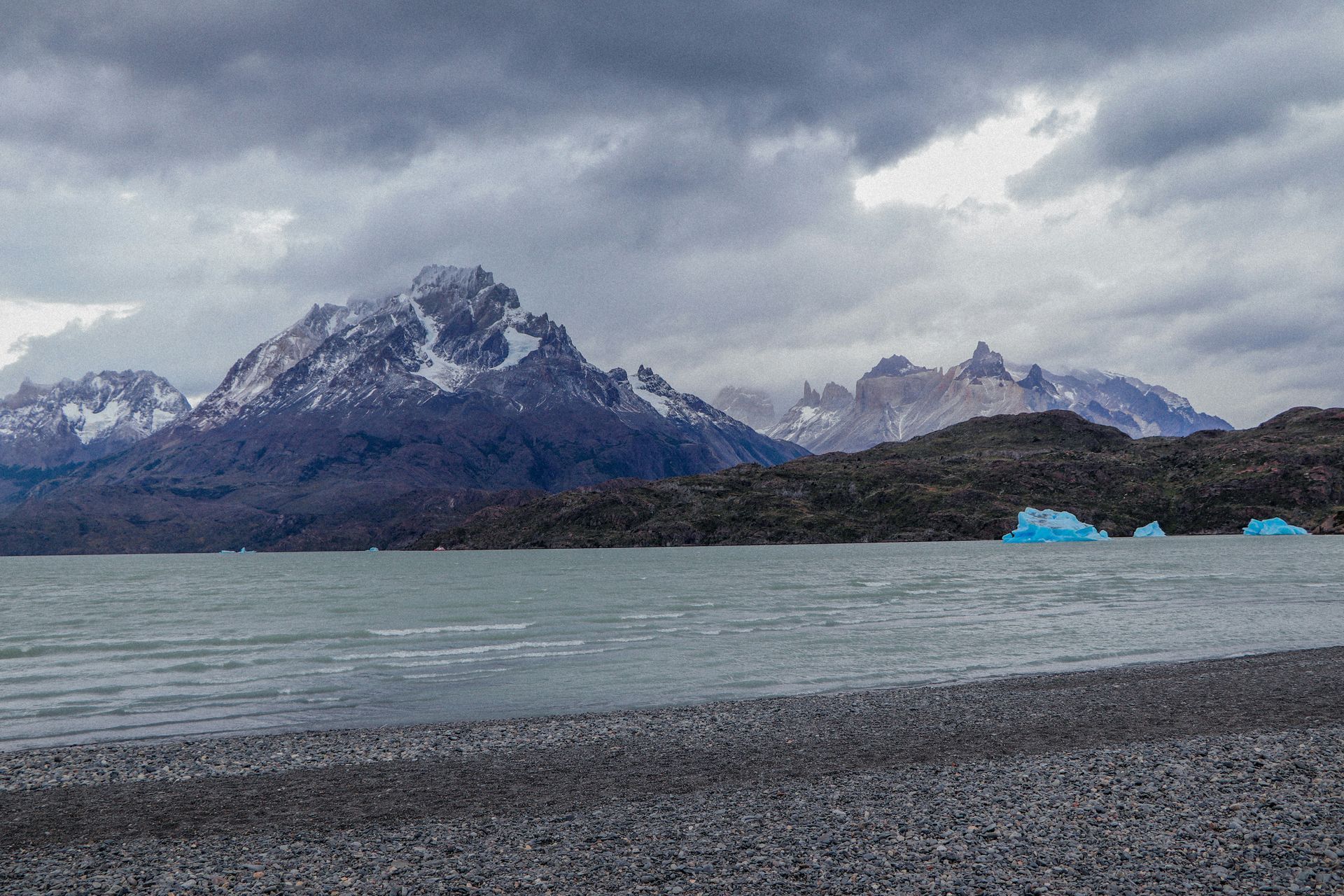 Lake shore with dark mountains, cloudy sky, and icy blue icebergs in Punta Arenas, Chile.