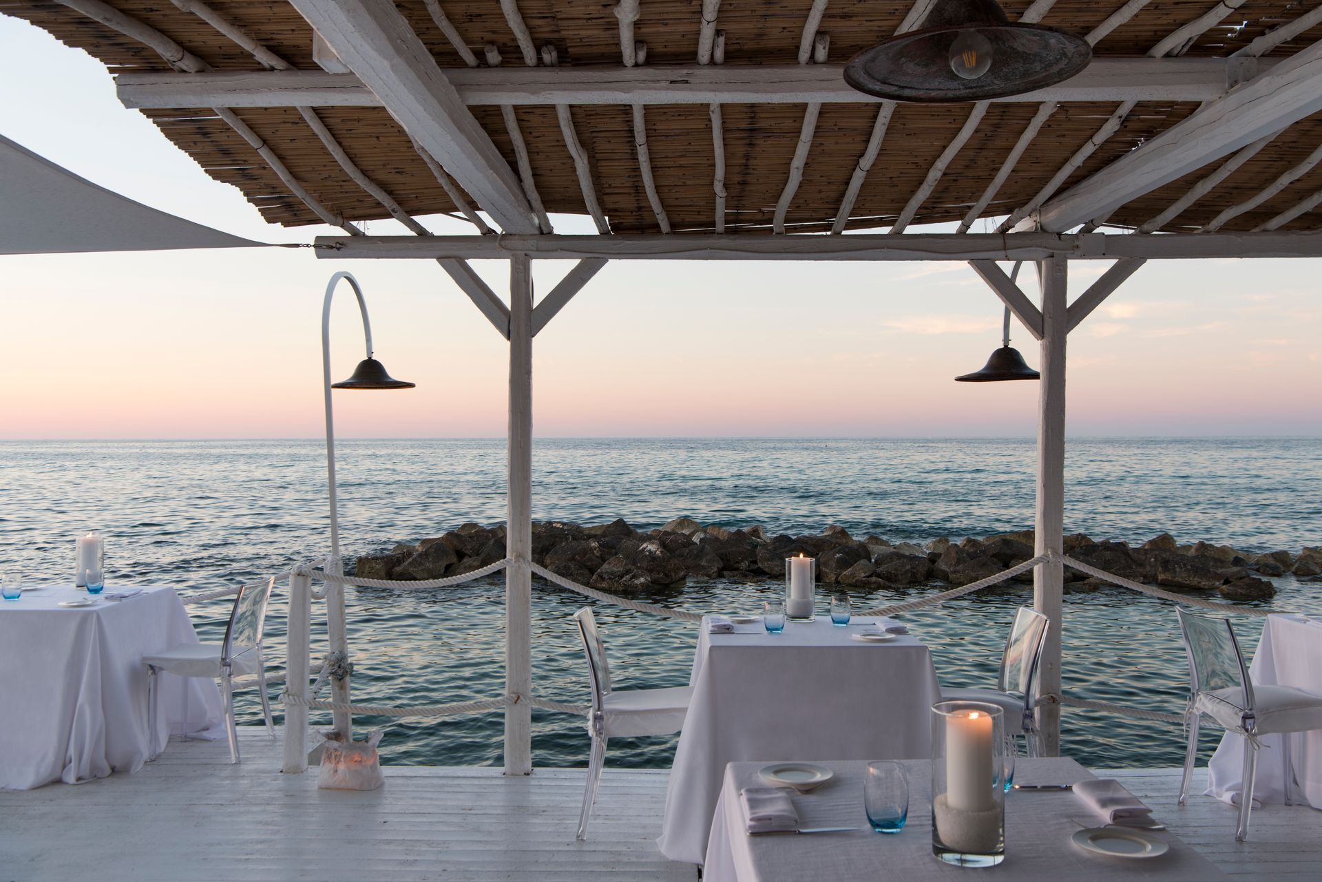 A restaurant with tables and chairs overlooking the ocean at La Peschiera Hotel in Puglia, Italy.