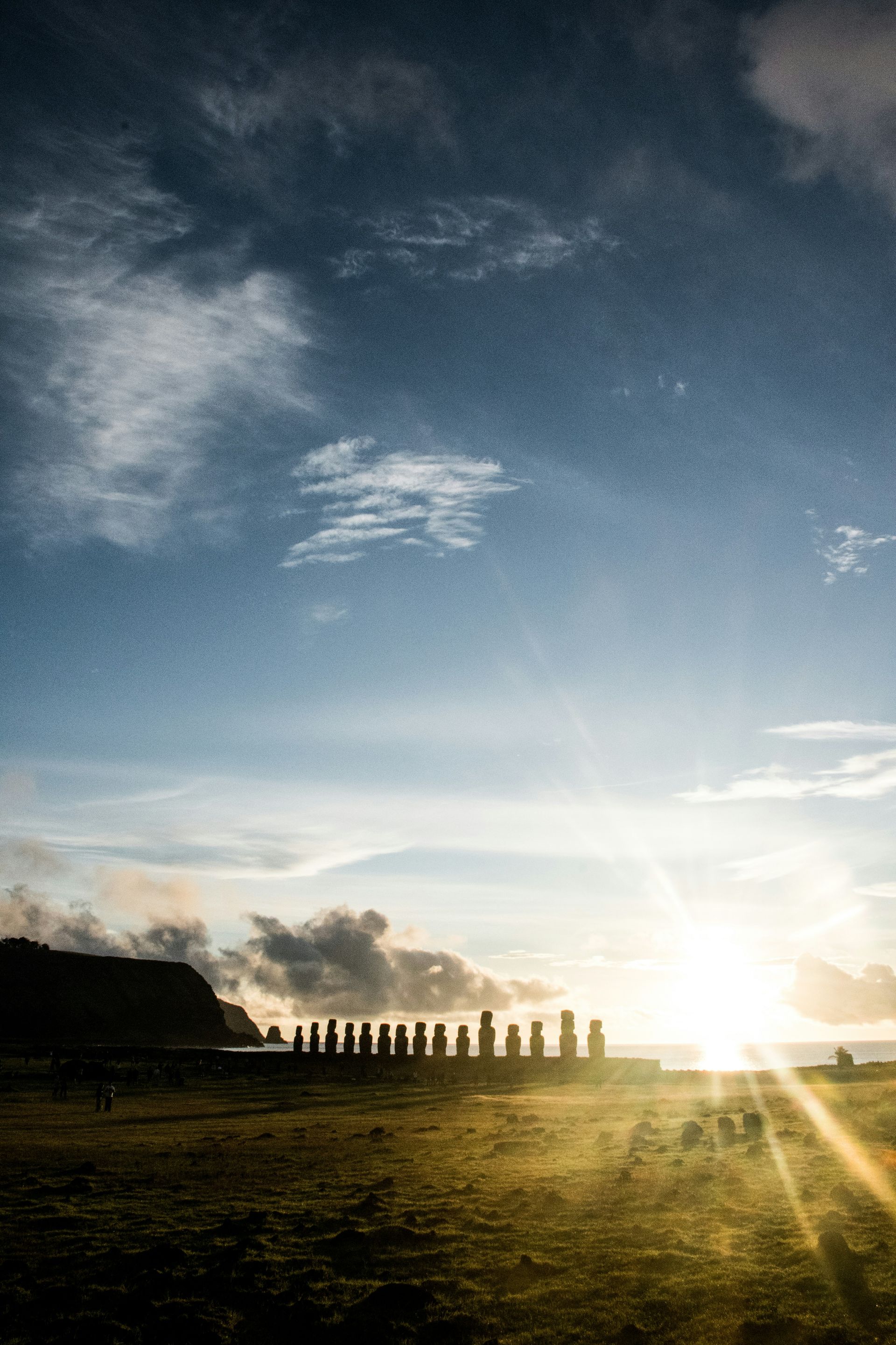 Moai statues silhouetted against a sunrise on Easter Island, with a blue sky and golden light.