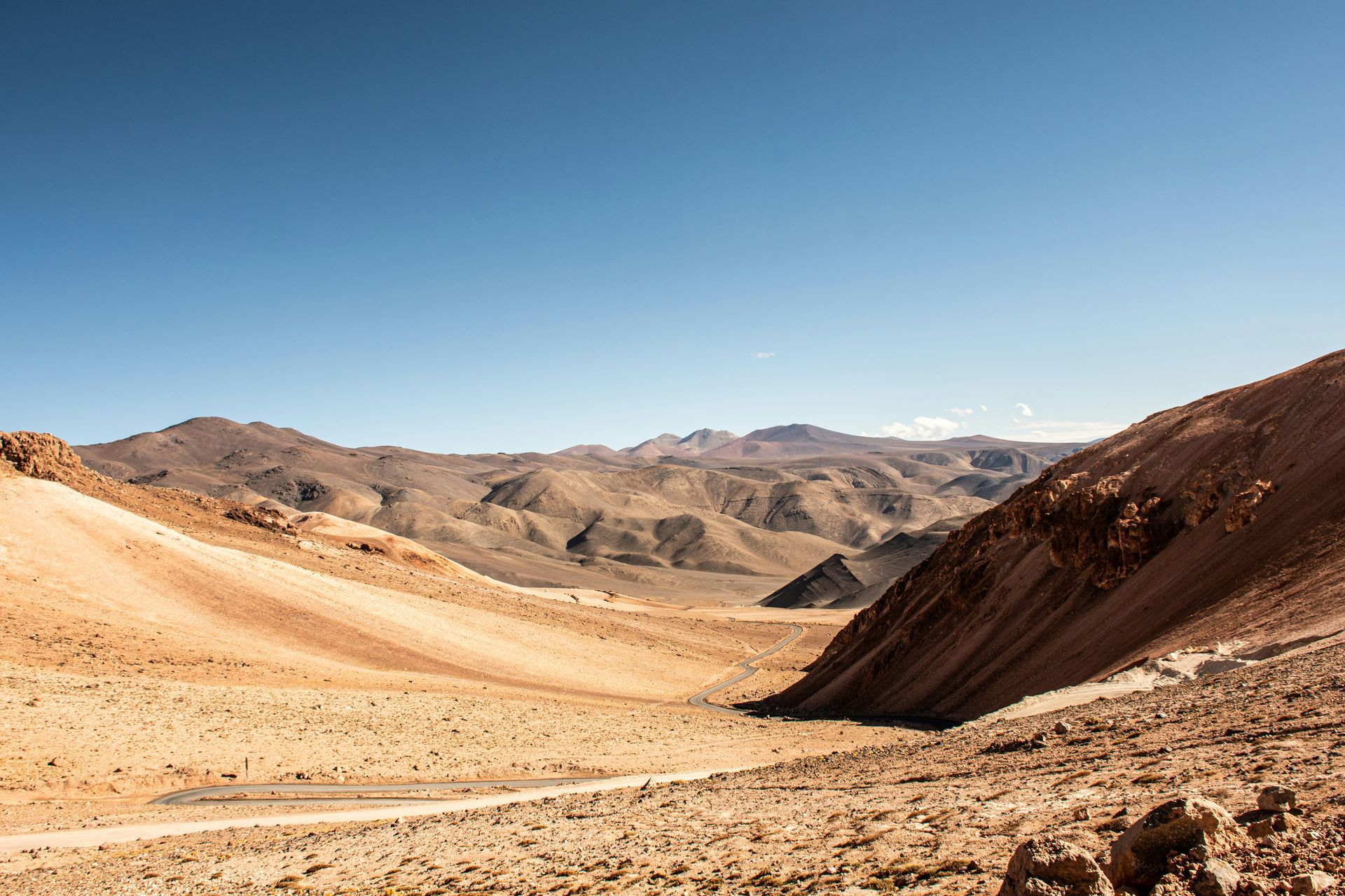Arid desert landscape with tan hills and mountains under a clear blue sky in the Atacama Desert, Chile.