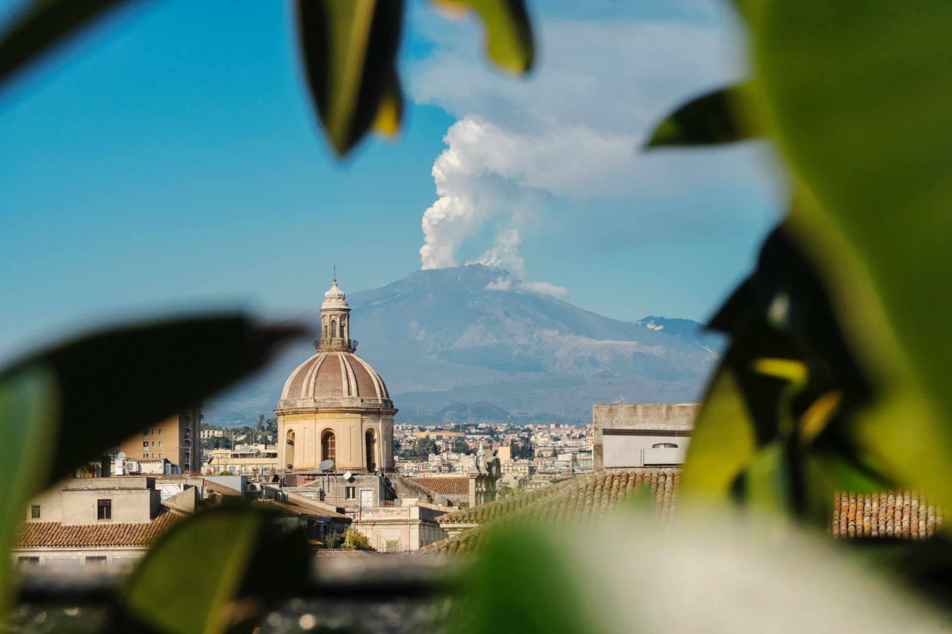A view of a city with a dome in the foreground and the volcano Mount Etna in the background in Sicily.