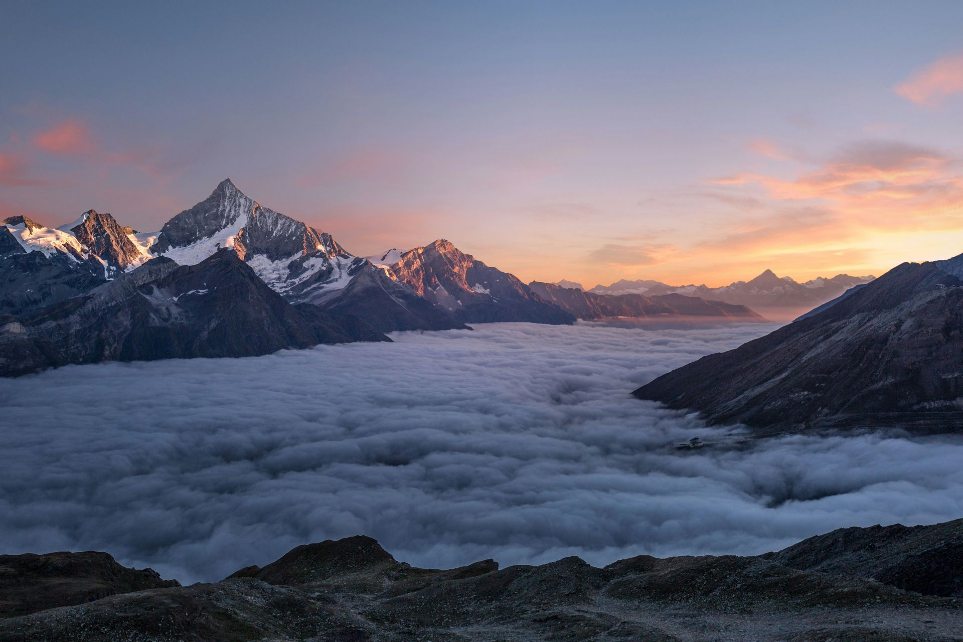 Mountains peak above a sea of clouds at dawn, with pink and orange sky in Switzerland.
