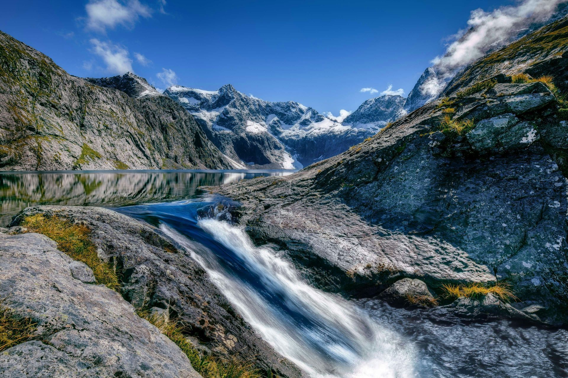 There is a waterfall in the middle of the mountains in Fiordland National Park, New Zealand.