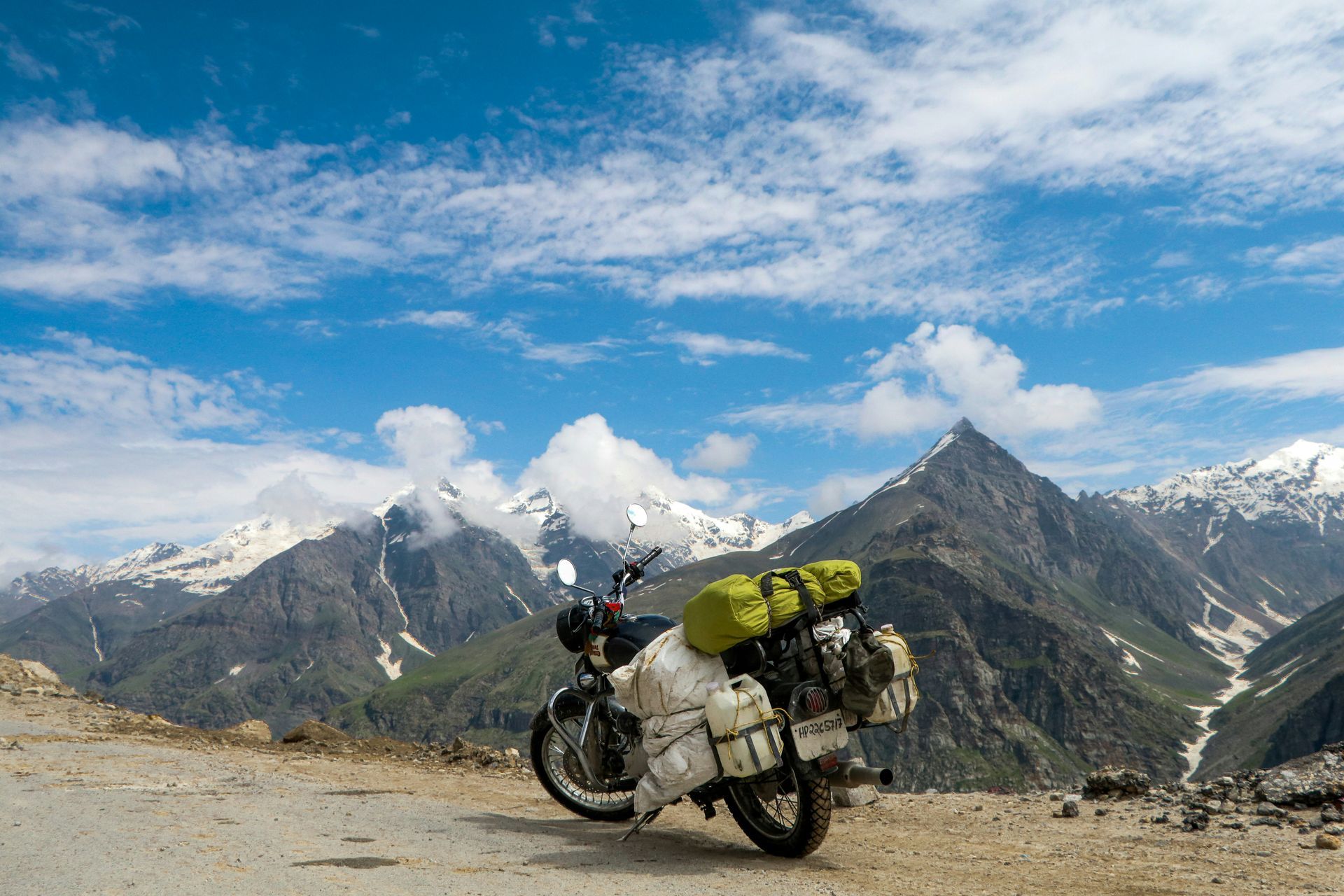 Motorcycle loaded with gear on a mountain road; snow-capped peaks in Ladakh, India.