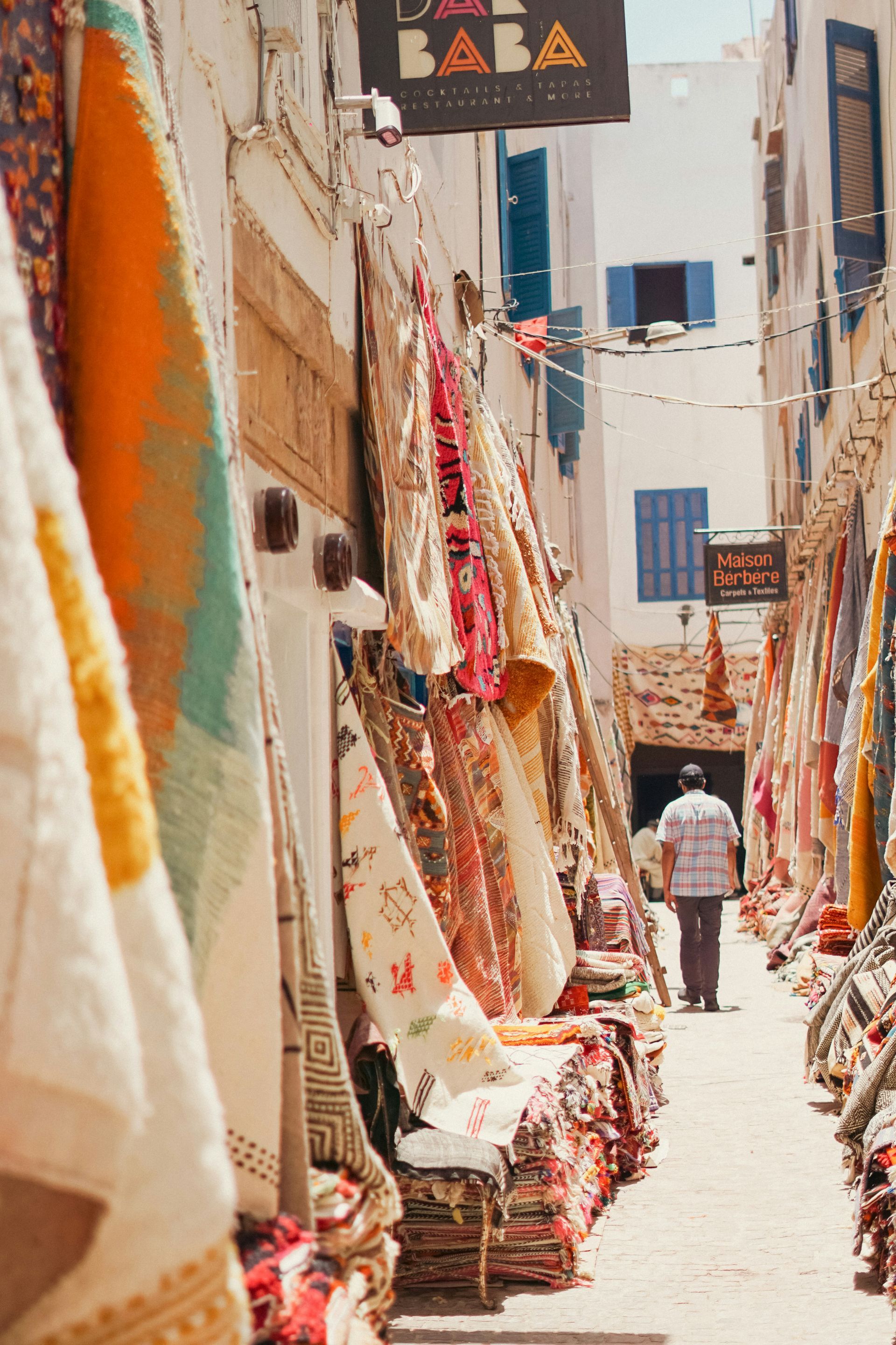A narrow street with a market selling colorful blankets on it in Essaouira, Morocco.