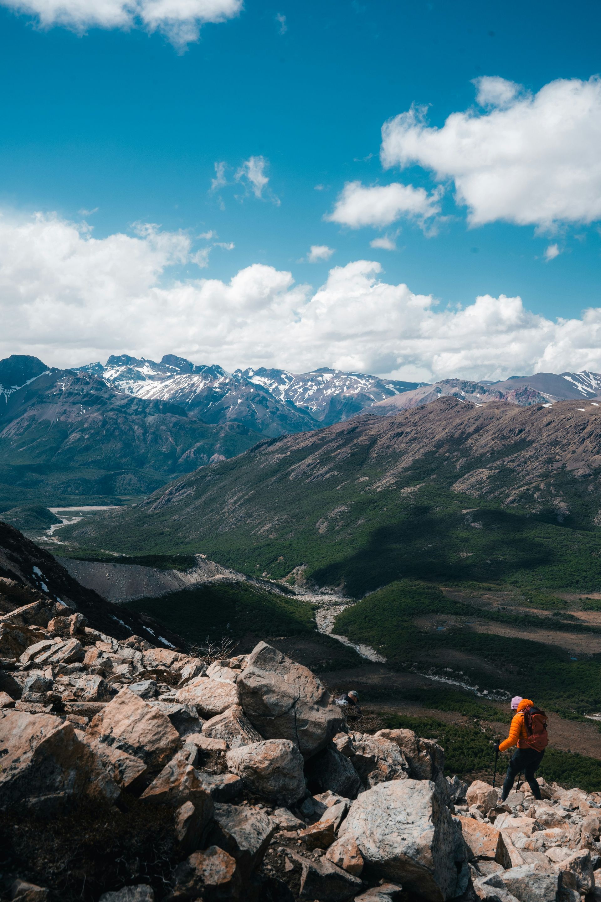 An overlook of a mountain valley with snow-capped peaks, under a blue sky with clouds in El Chaltén, Argentina.