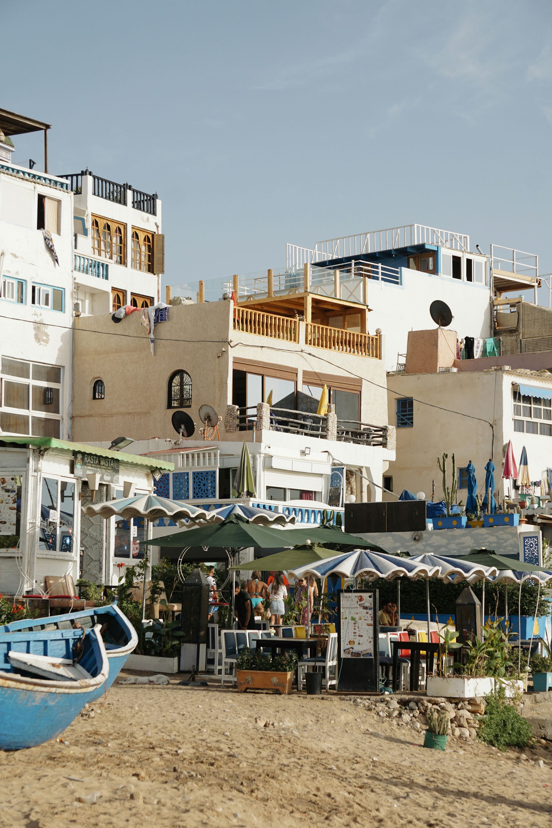 A boat is sitting on the beach in front of a row of buildings in Taghazout, Morocco.